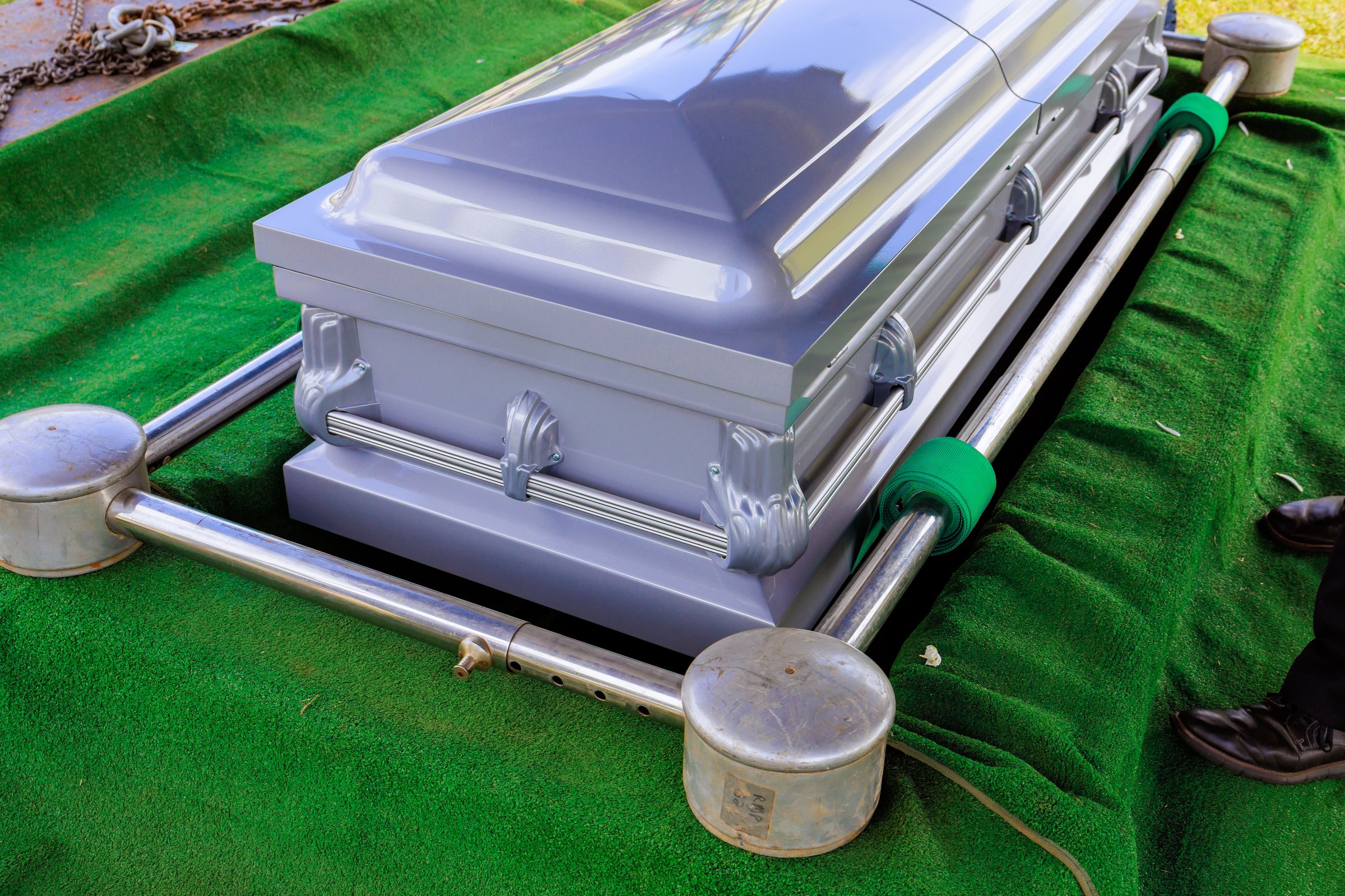 Gray metal coffin rests in grassy area of cemetery somber atmosphere solemnity during funeral preparation