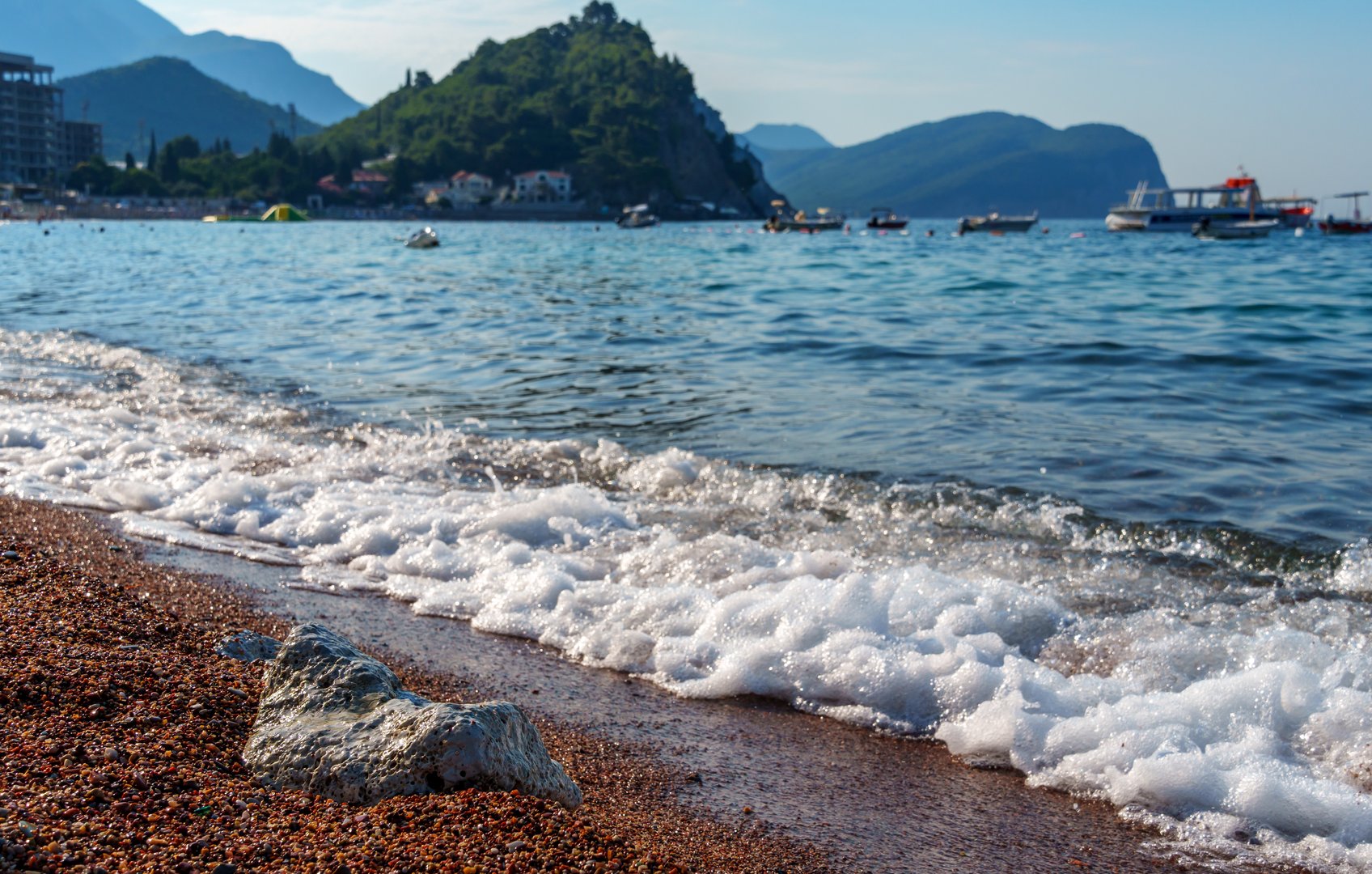 city beach with beautiful coastline and view of Adriatic sea in Petrovac, Montenegro, with high forested hills in the background