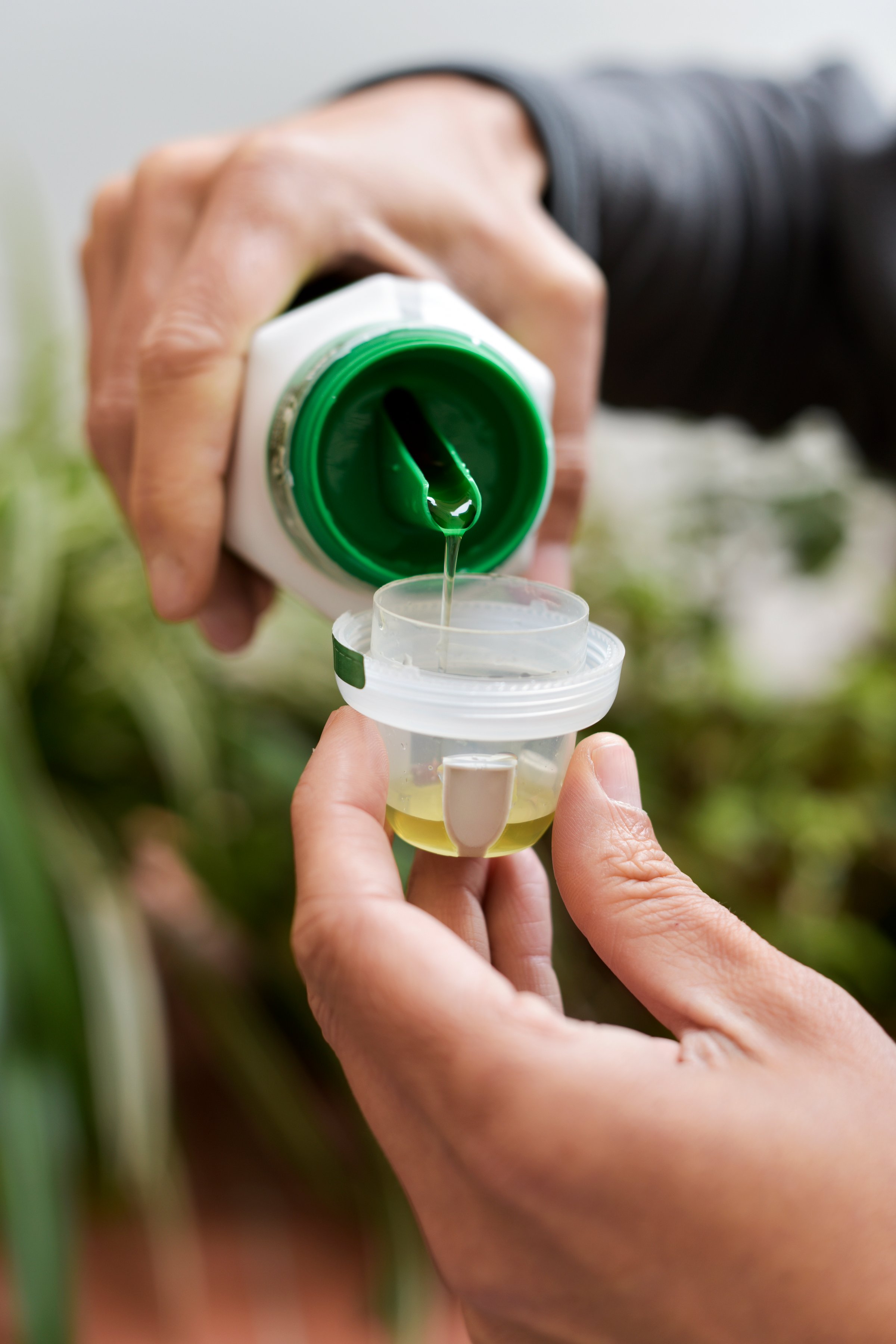 closeup of a young caucasian man outdoors measuring a dose of liquid fertilizer for his plants