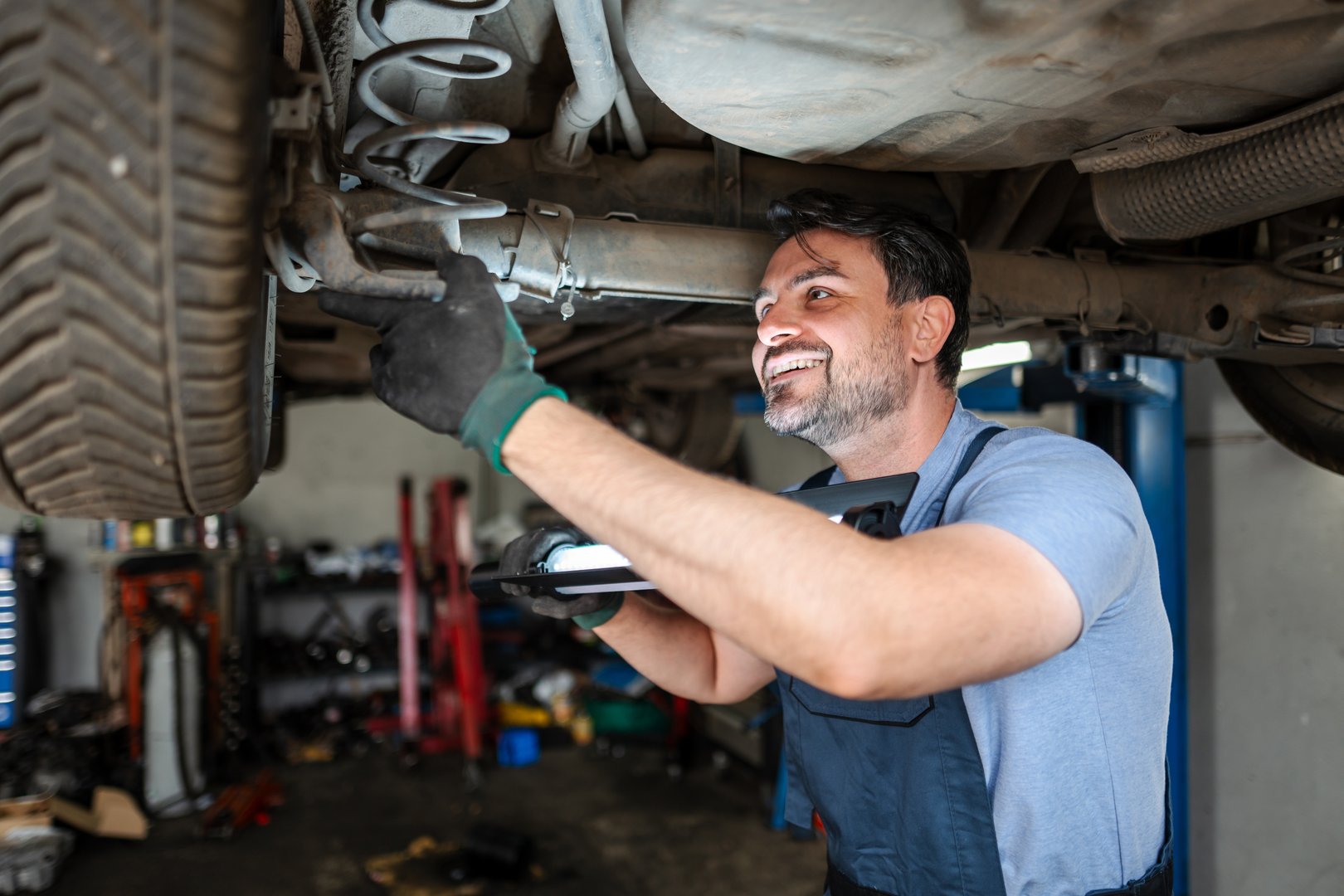 Smiling mechanic inspecting car suspension with led lamp in garage