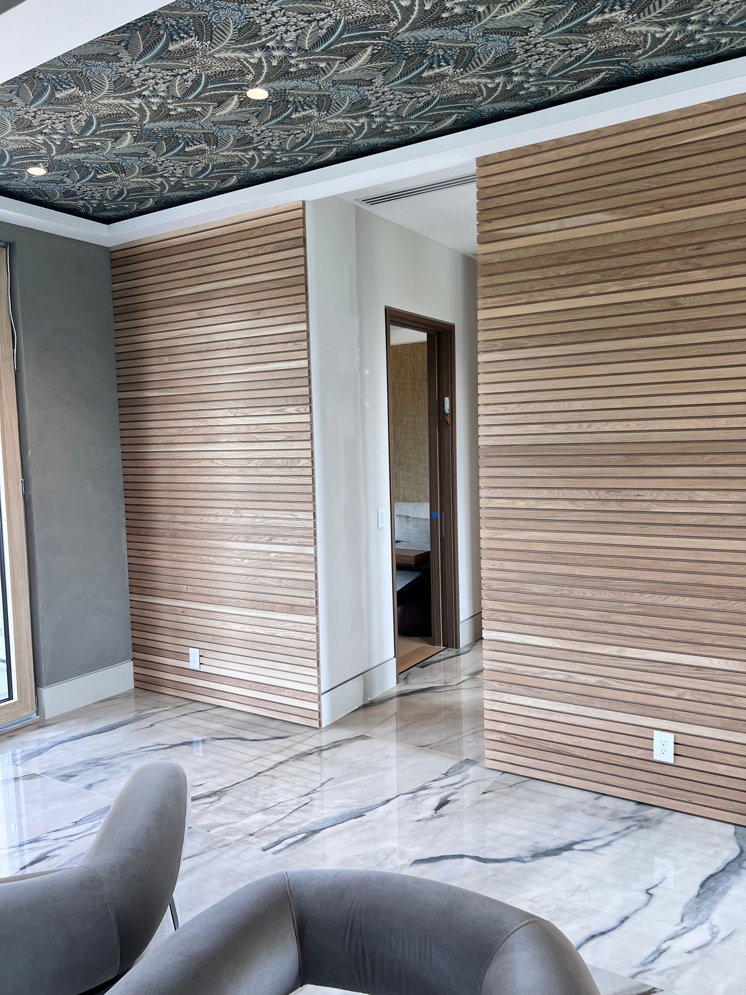 Modern room with sleek marble floor, wooden slat wall panels, and a decorative patterned ceiling.
