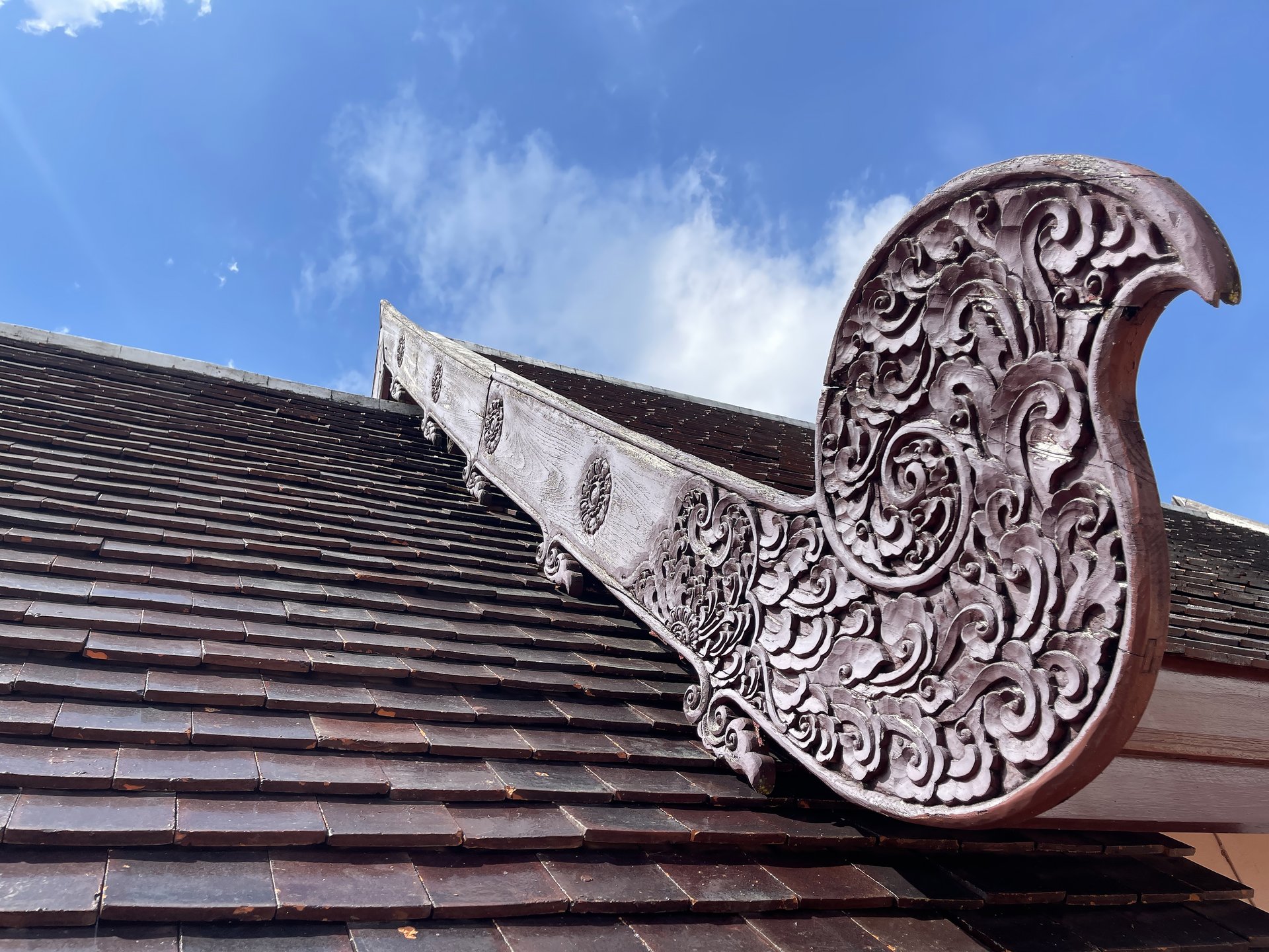 Ornate wooden roof detail with intricate carvings against a blue sky.