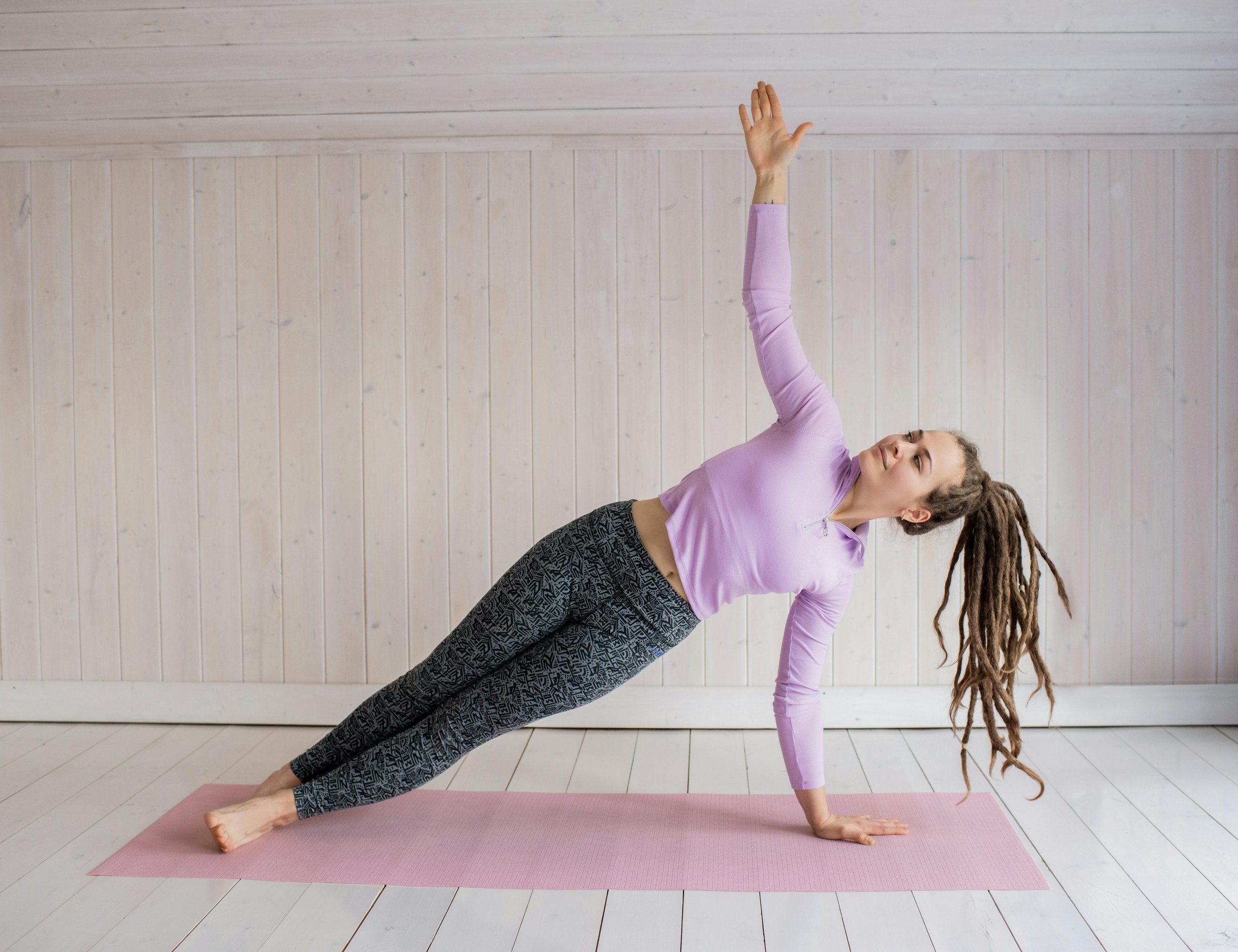 Pilates instructor guides her student through a challenging stretching exercise on a reformer machine in a modern pilates studio