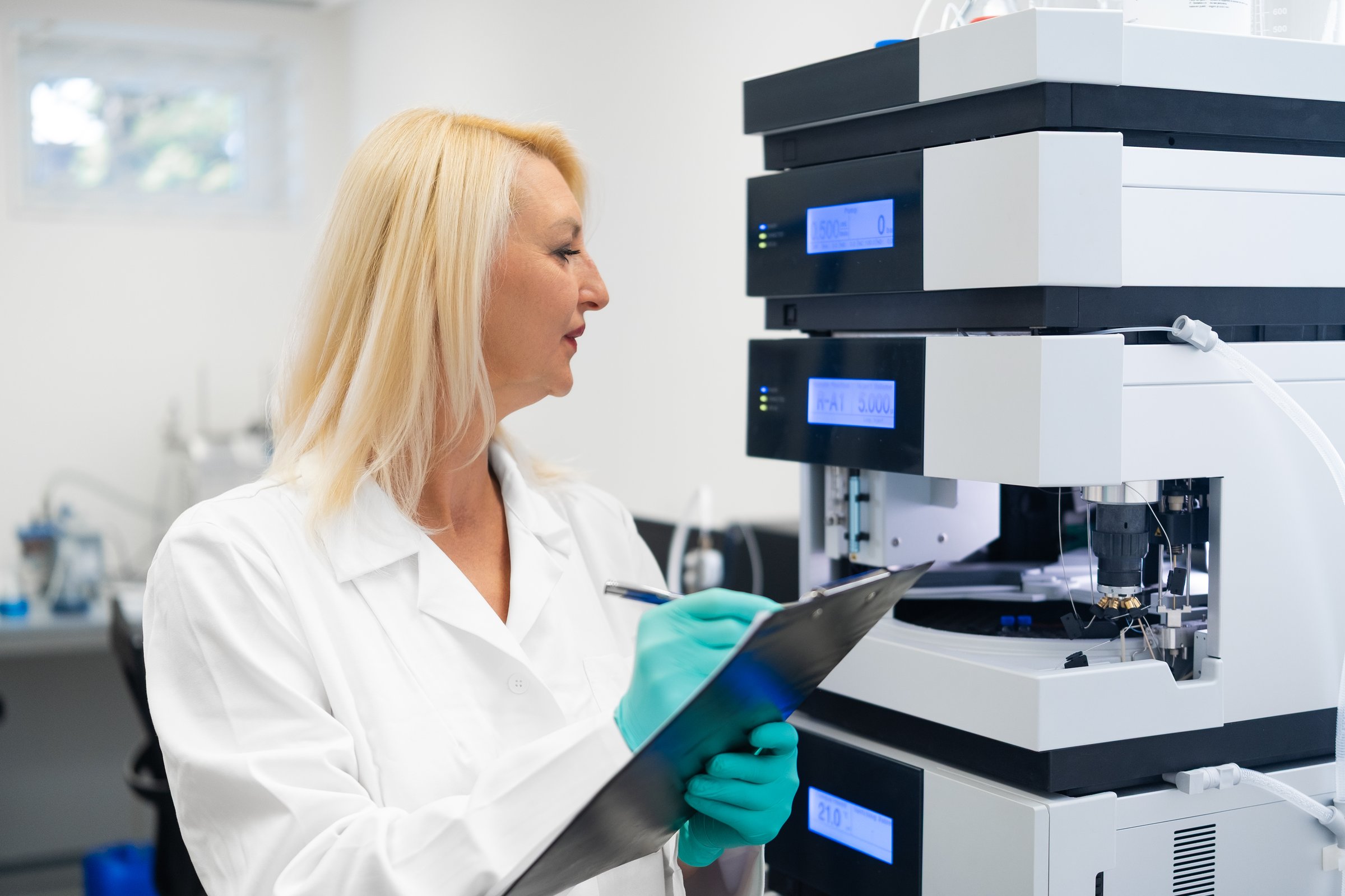 Senior female scientist in lab coat documenting results of HPLC analysis in a chemical laboratory. Concept of research, accuracy, and professional science.