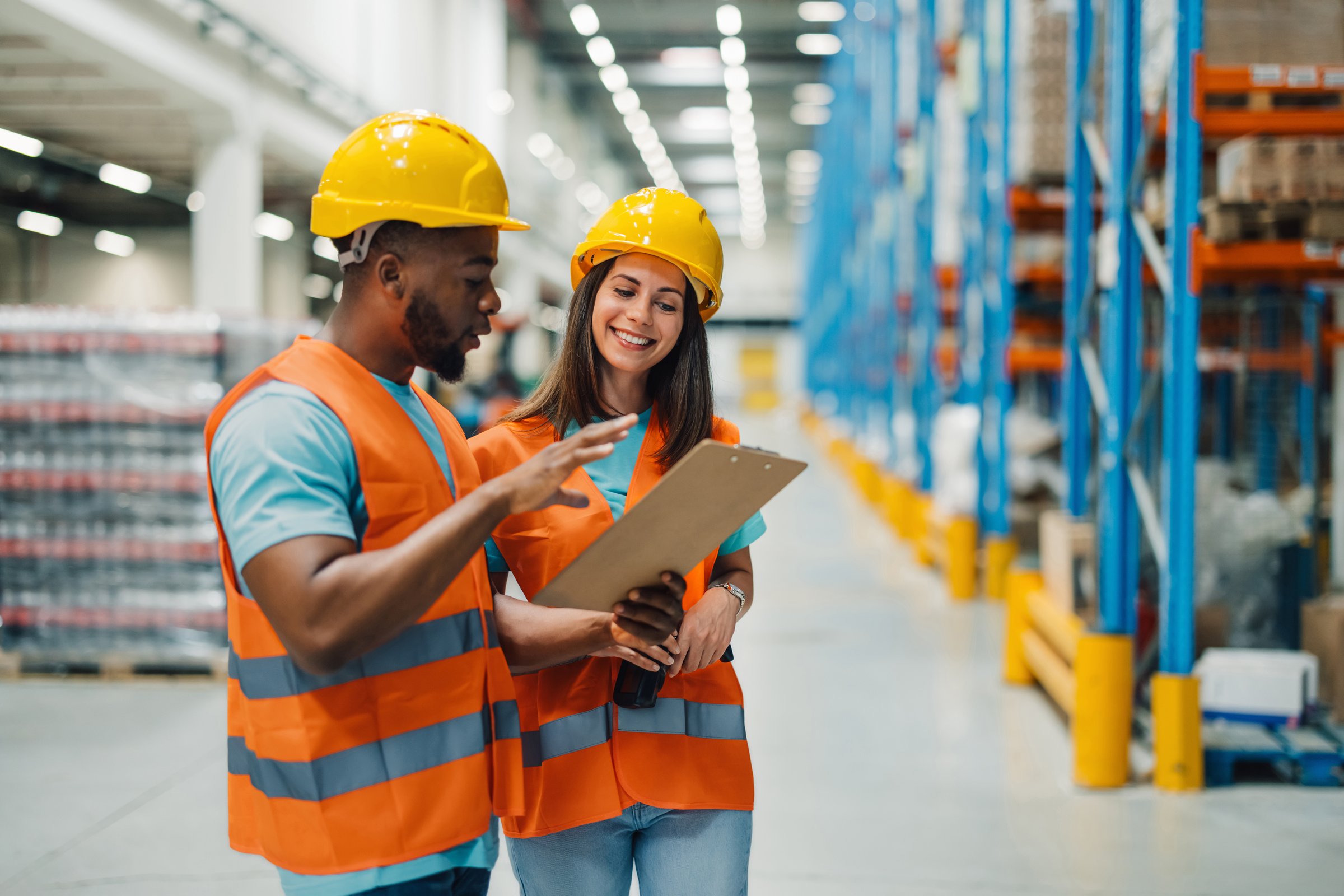 Two diverse warehouse workers are reviewing inventory and logistics inside a large distribution warehouse center, optimizing their workflow for efficiency