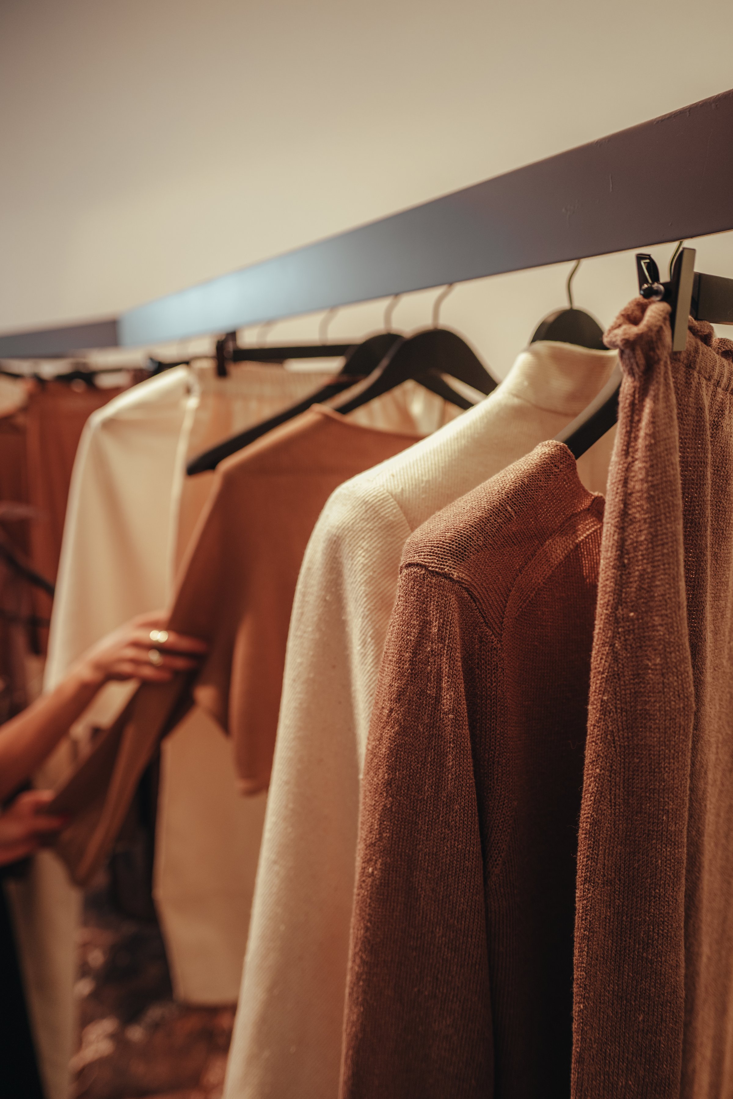 Women's stylish clothes in brown, beige neutral colors hanging in a row in a fashionable luxury boutique
