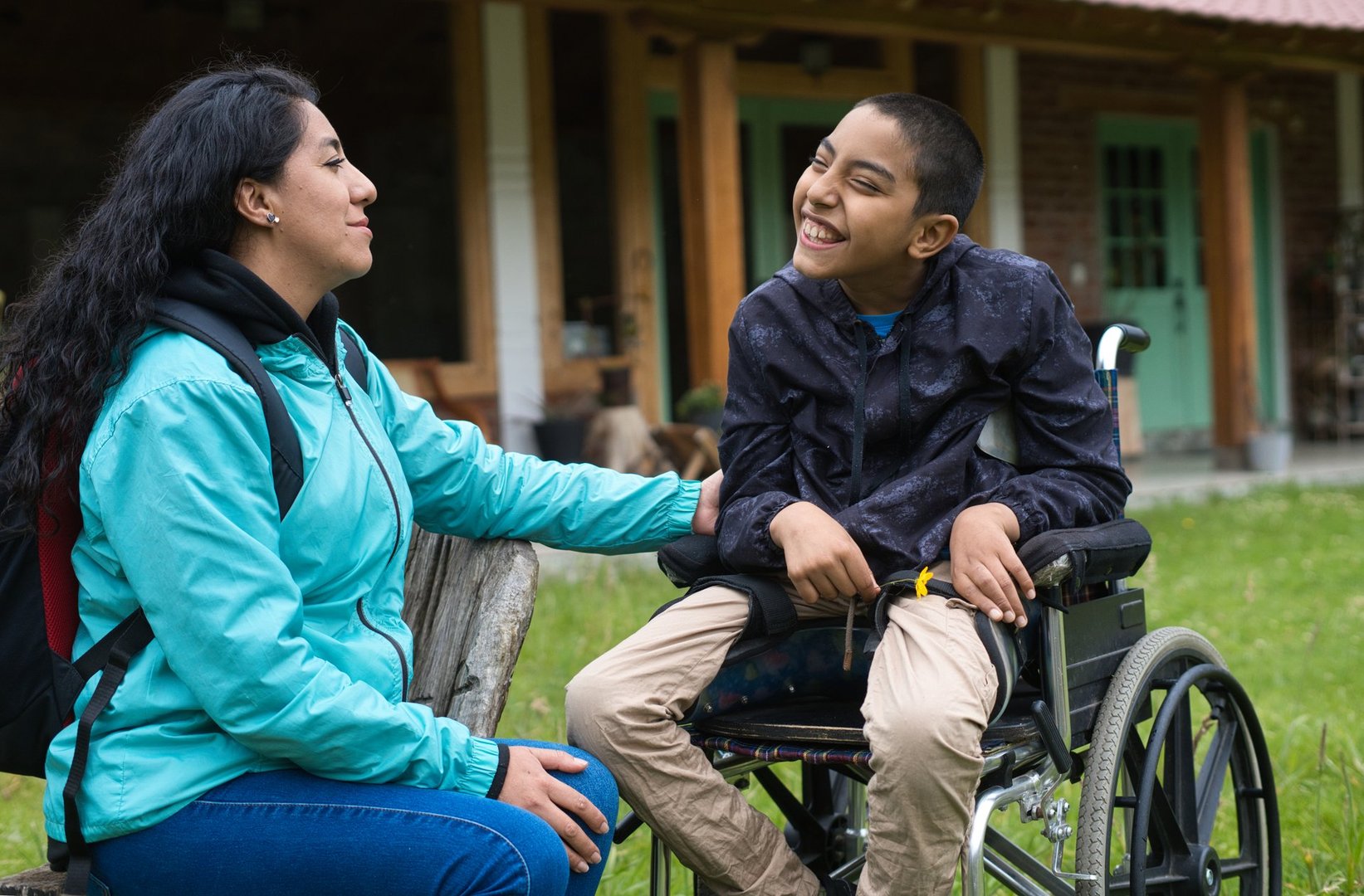 Latin american mother taking care of her happy disabled preteen son in a wheelchair, enjoying a day outdoors in the garden of a country house, promoting inclusive tourism