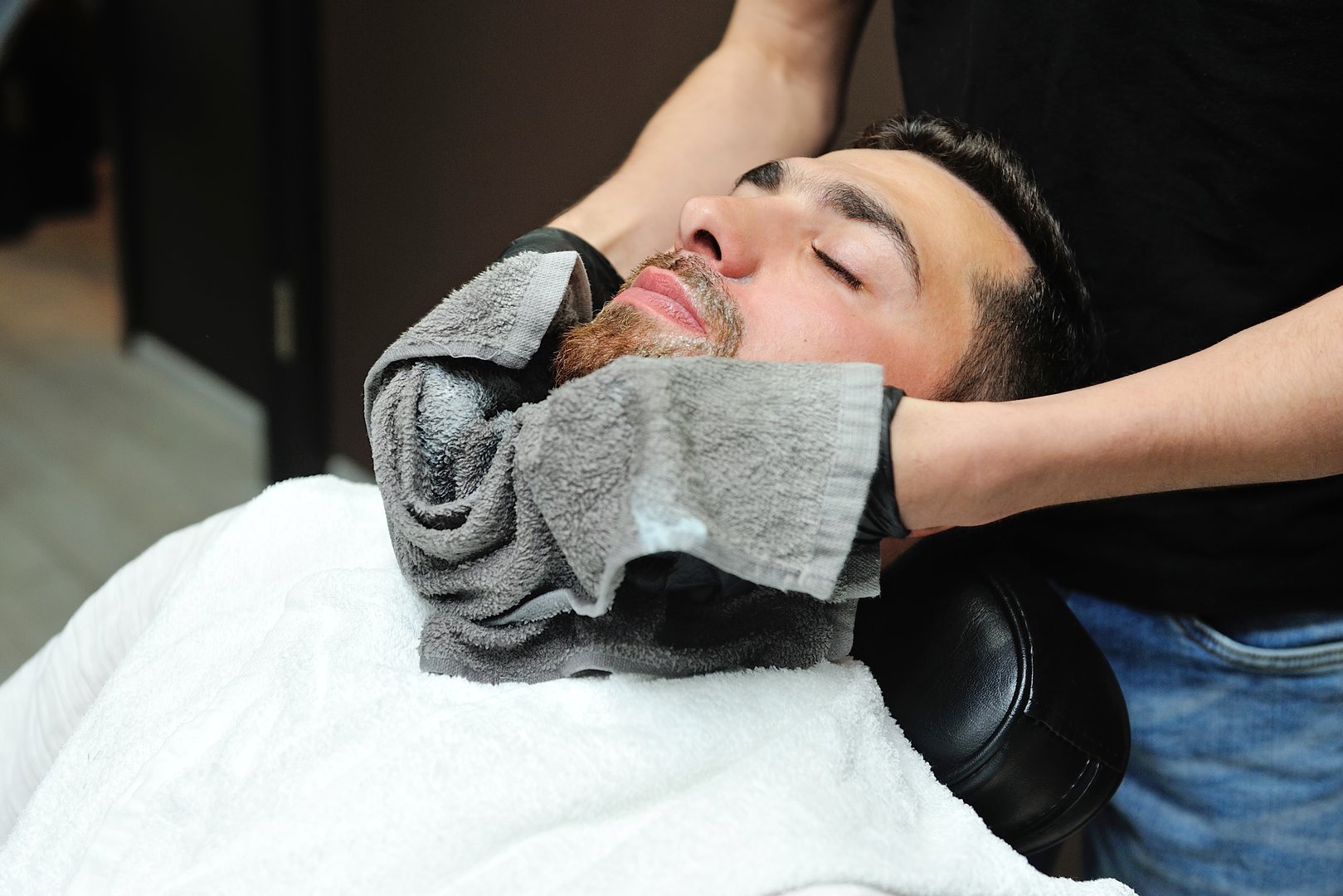 Barber preparing man face for shaving with hot towel on face in barber shop.