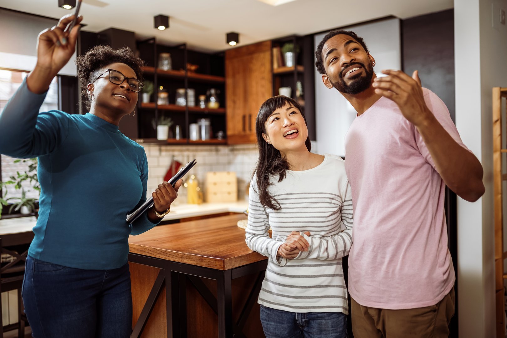 African American real estate agent showing house to multiracial couple, real estate agent telling clients about home advantages, interior designer discussing renovation ideas with homeowners.