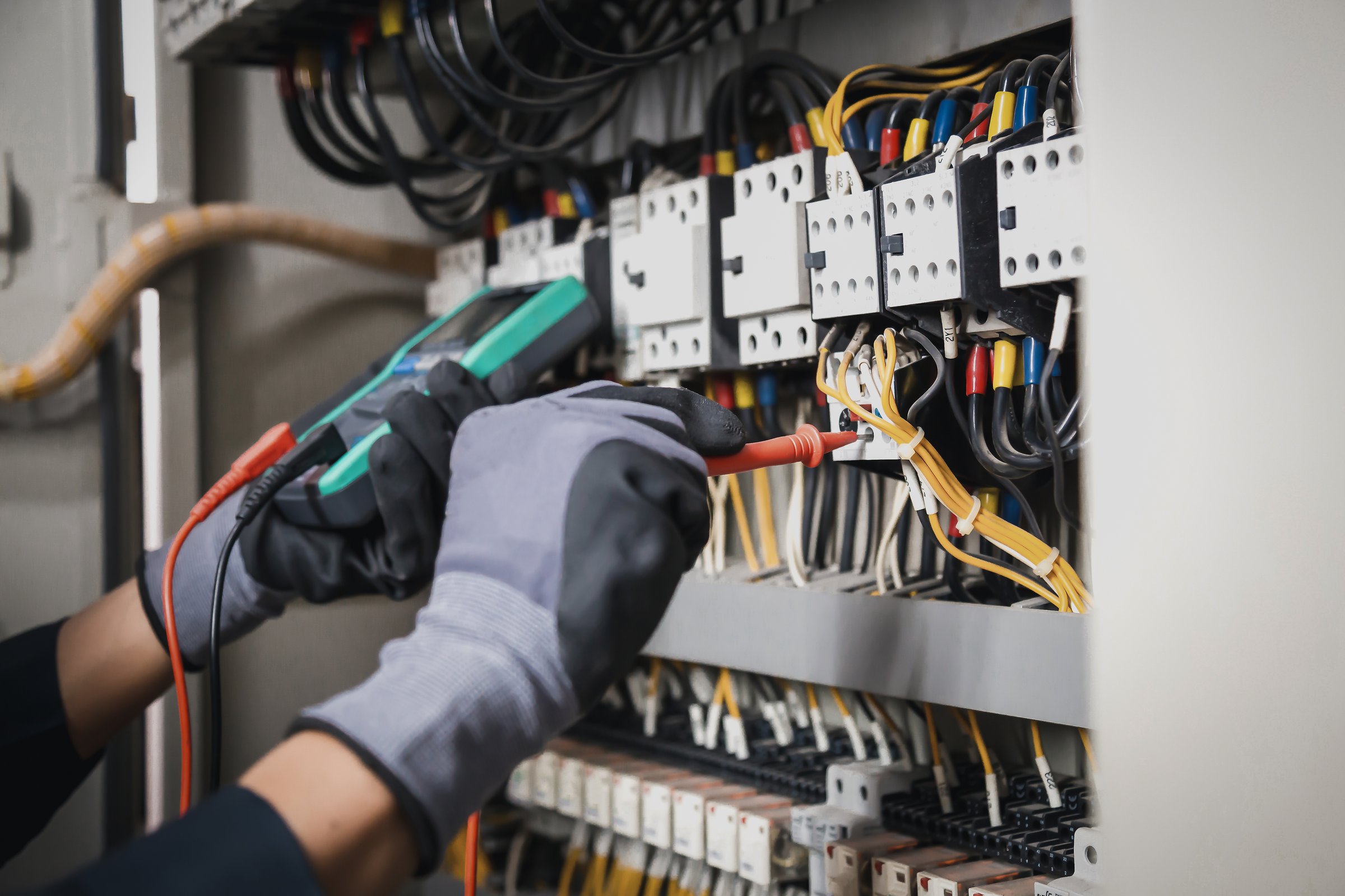 Electricity and electrical maintenance service, Engineer hand holding AC multimeter checking electric current voltage at circuit breaker terminal and cable wiring main power distribution board.