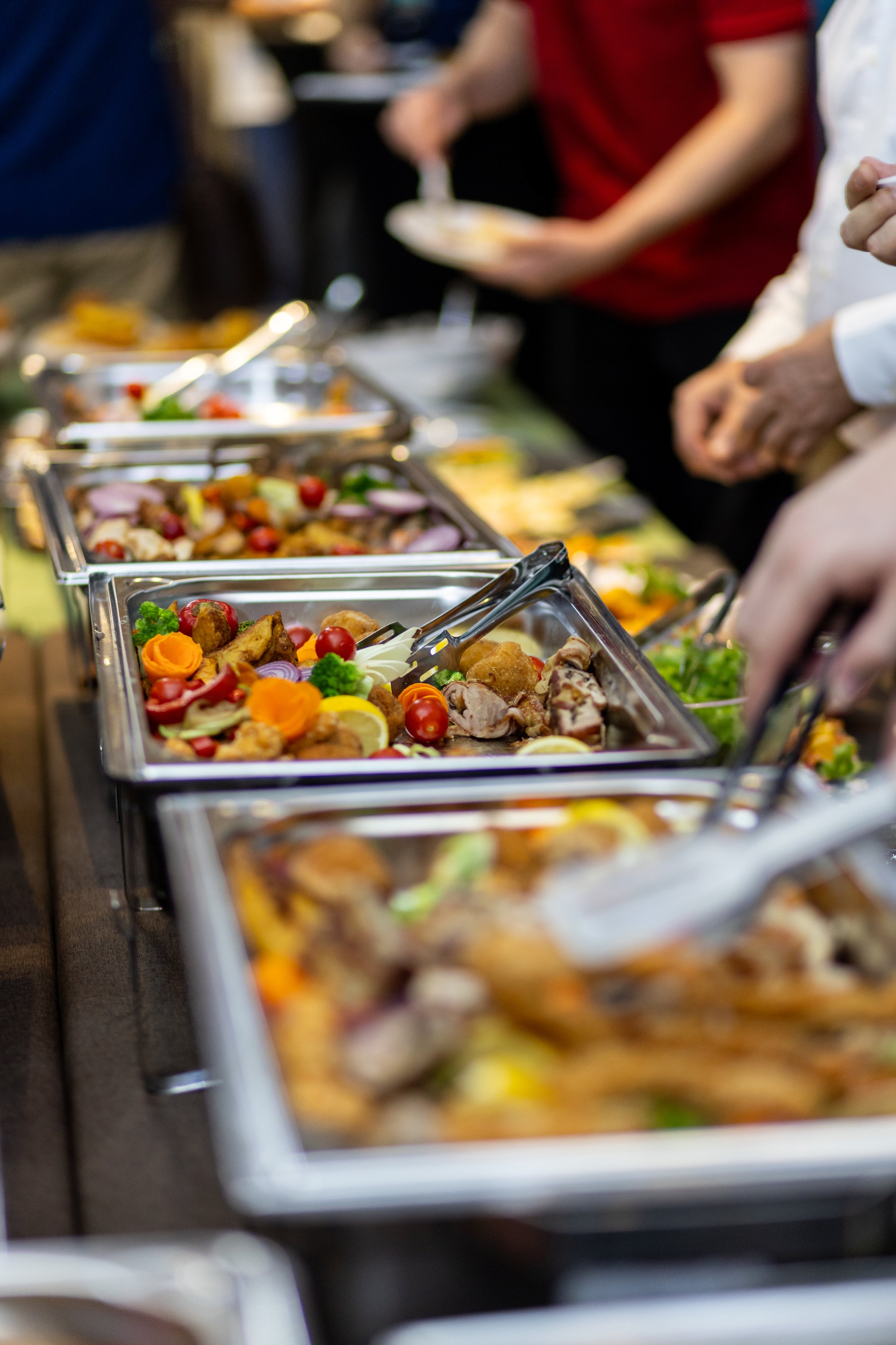 Guests eagerly serve themselves from a well-stocked buffet, showcasing colorful salads and various meat dishes, creating a festive dining atmosphere during an event.