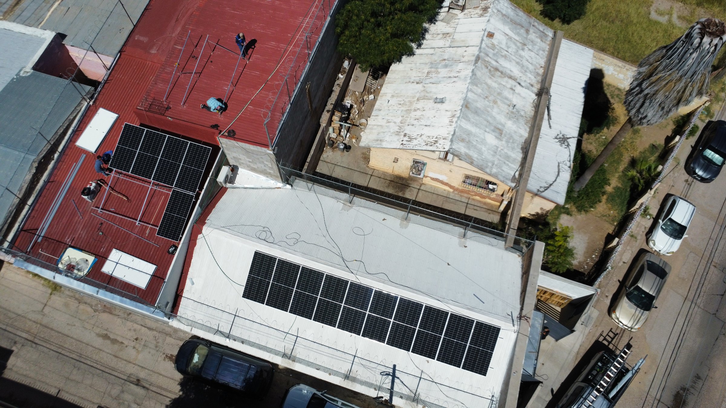 Aerial view of solar panels being installed on the rooftops of two neighboring buildings in an urban area.