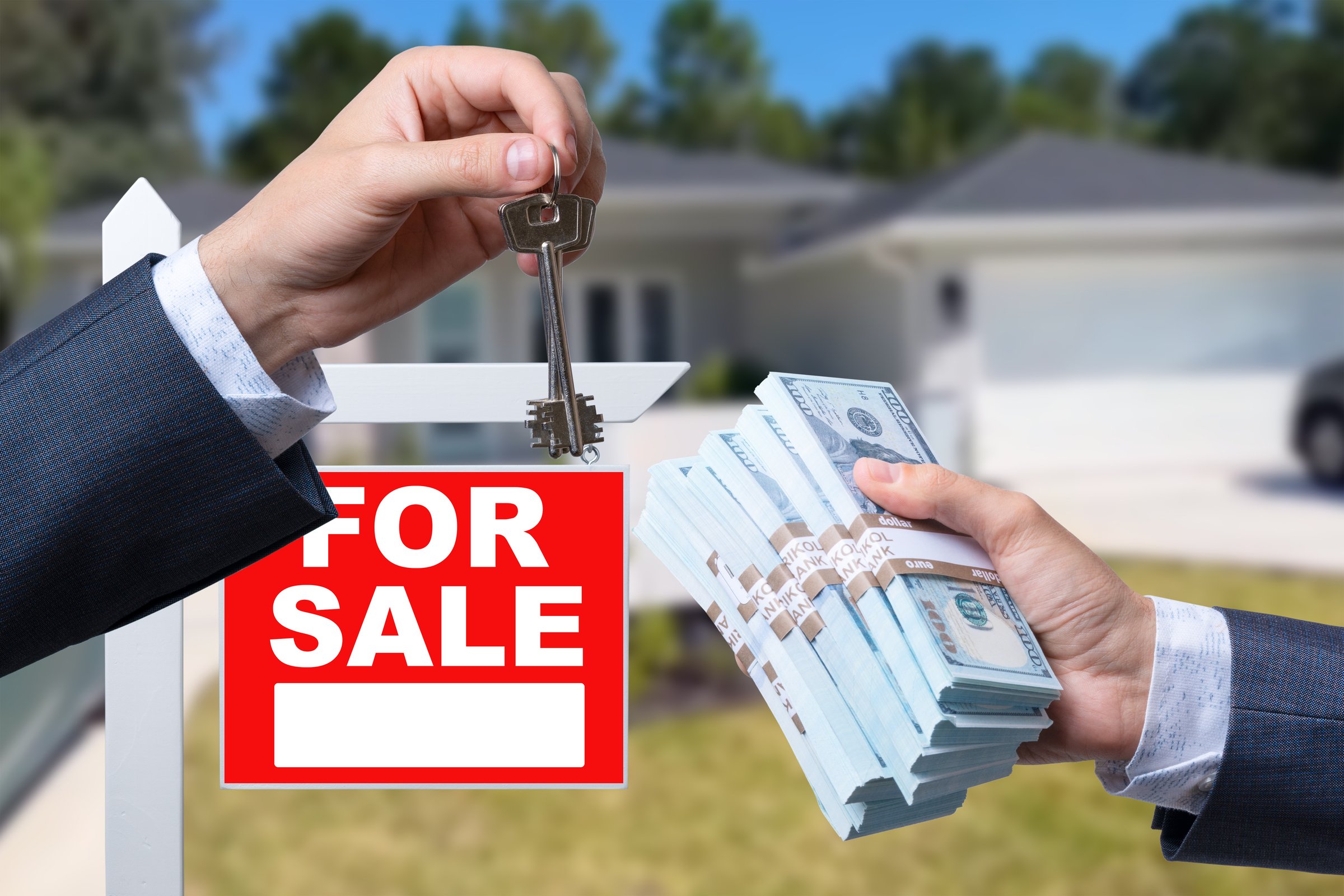 Agent Handing Over Keys as Buyer is Handing Over Cash for House with Home and For Sale Real Estate Sign Behind.