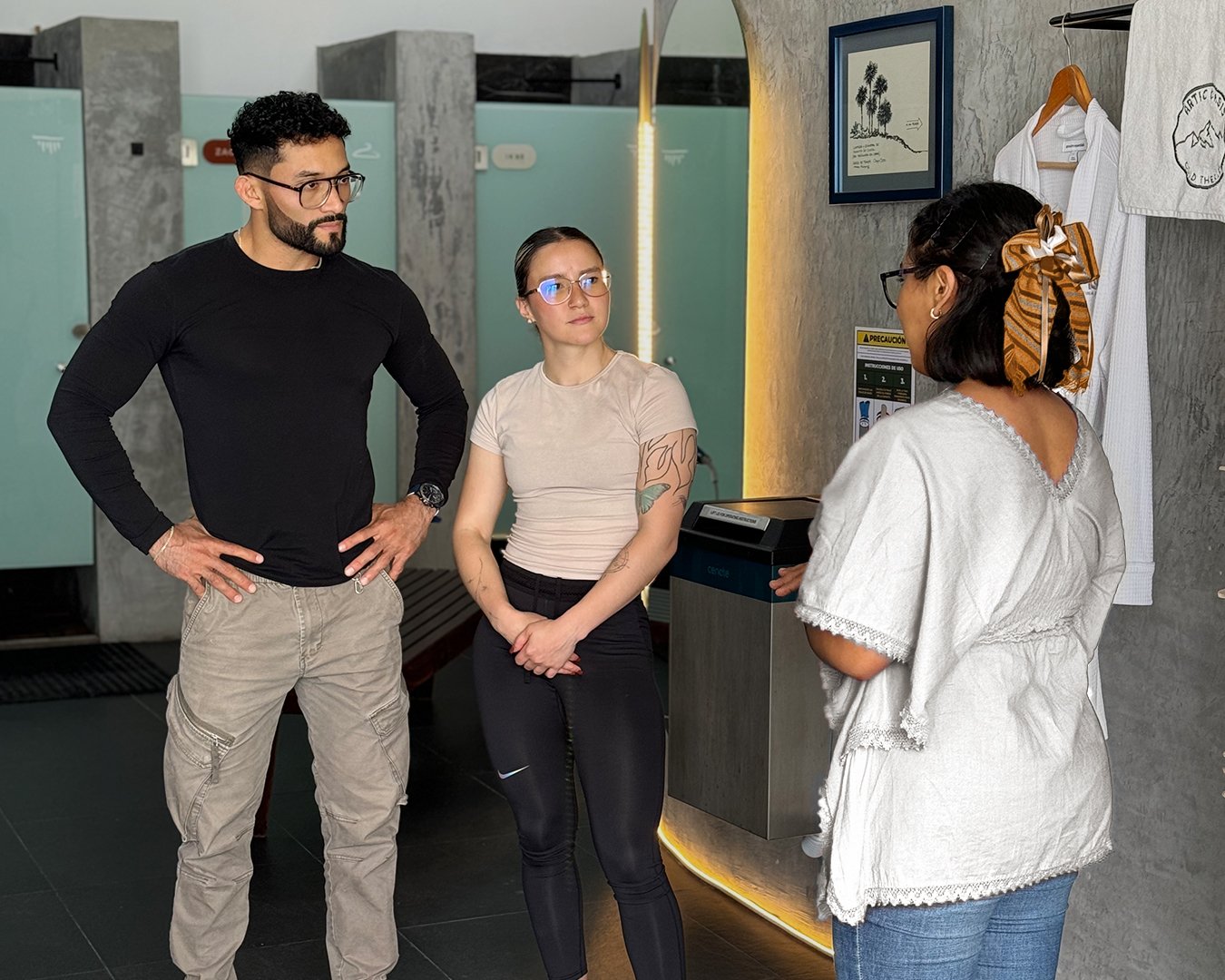 Three people stand in a casual conversation in a modern indoor setting, with a towel on the wall and decor in the background.