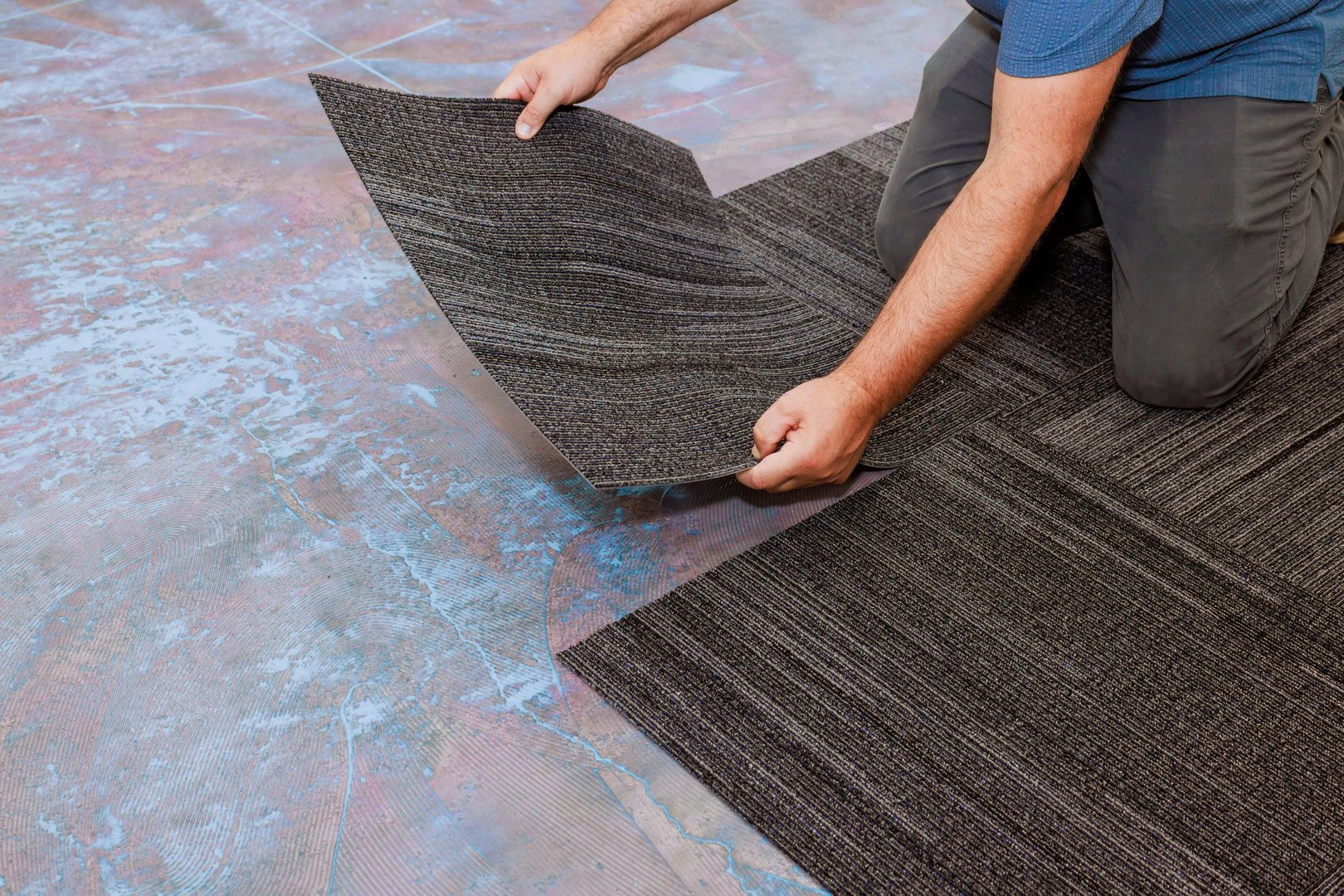 Man on his knees places carpet tiles on colorful floor, ensuring they fit snugly together