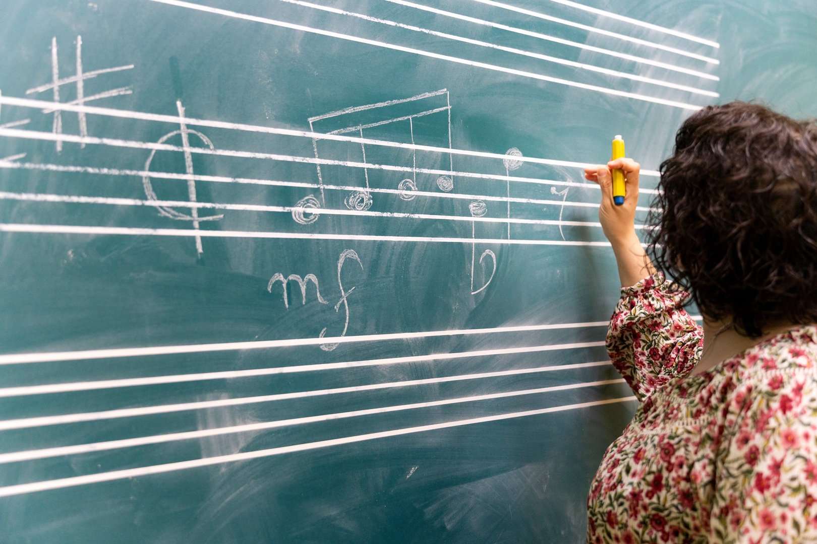Music teacher writing musical notes on a chalkboard with yellow chalk during a music theory lesson