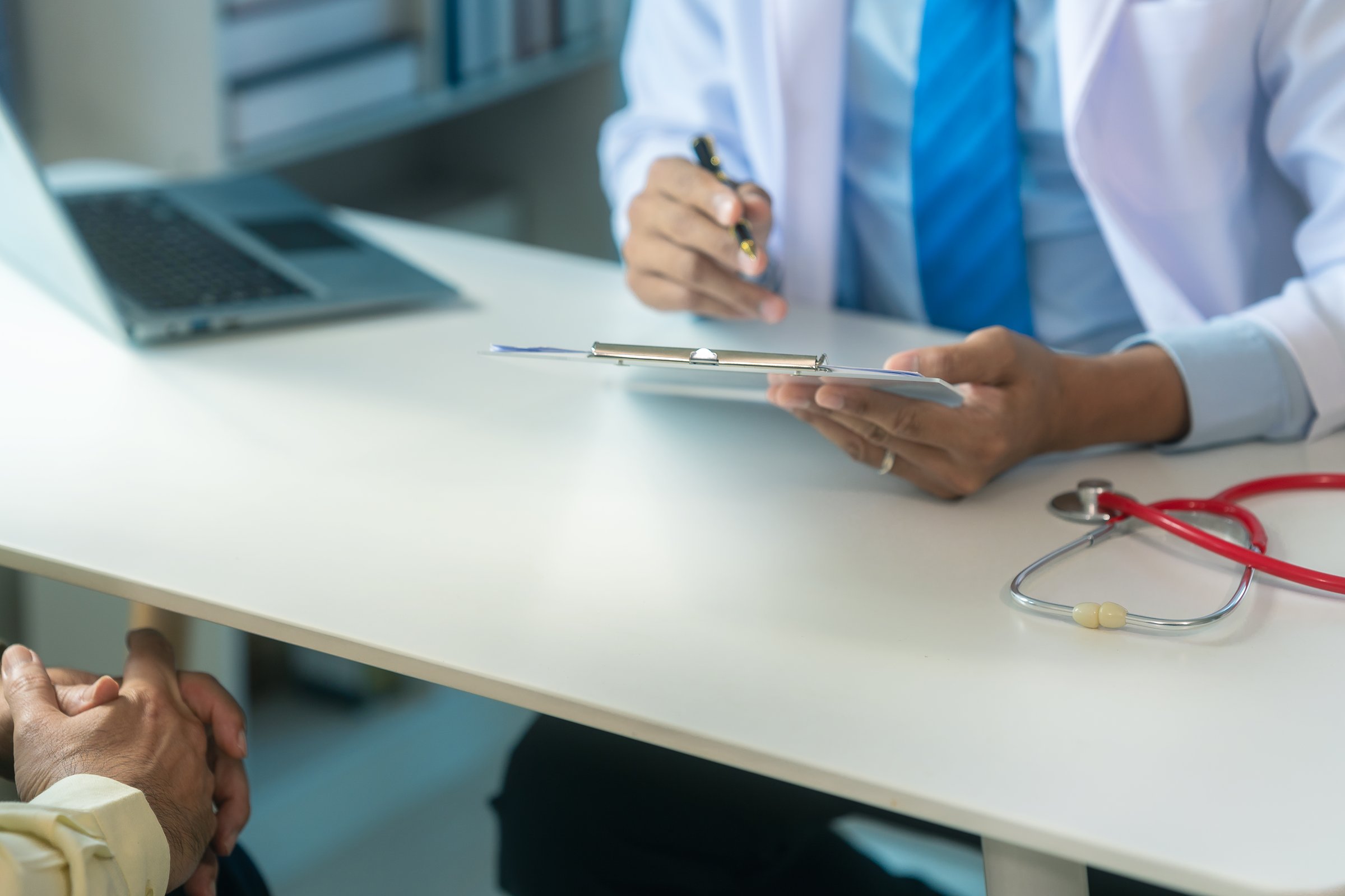 Asian orthopaedic surgeon provides consultation and explanation of knee model to male patient with focus on diagnosis, geriatric care and rehabilitation support.