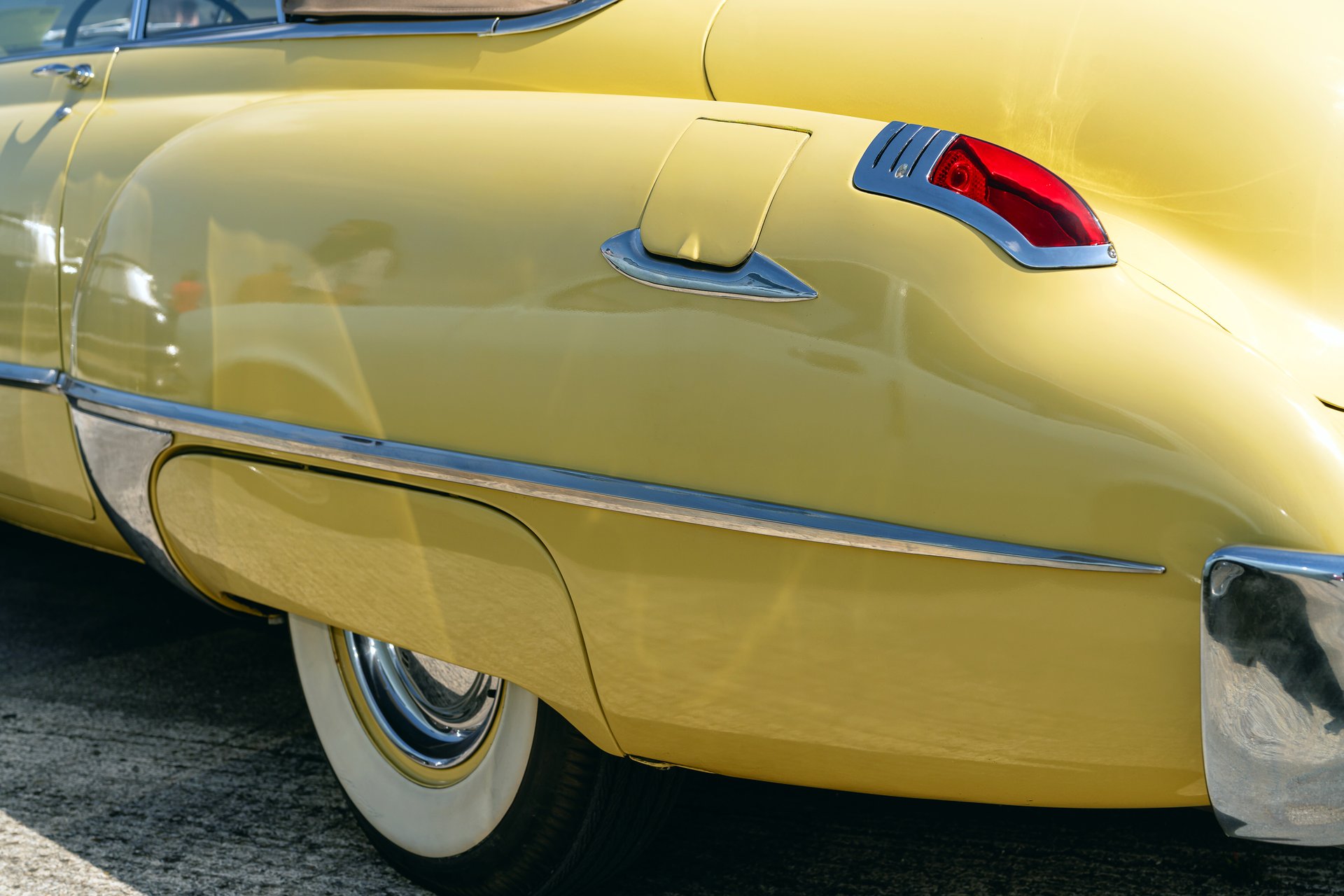Rear view of a vintage yellow automobile showcasing chrome trim, elegant curves, and retro tail lights. Featuring whitewall tires for a timeless classic car appeal.