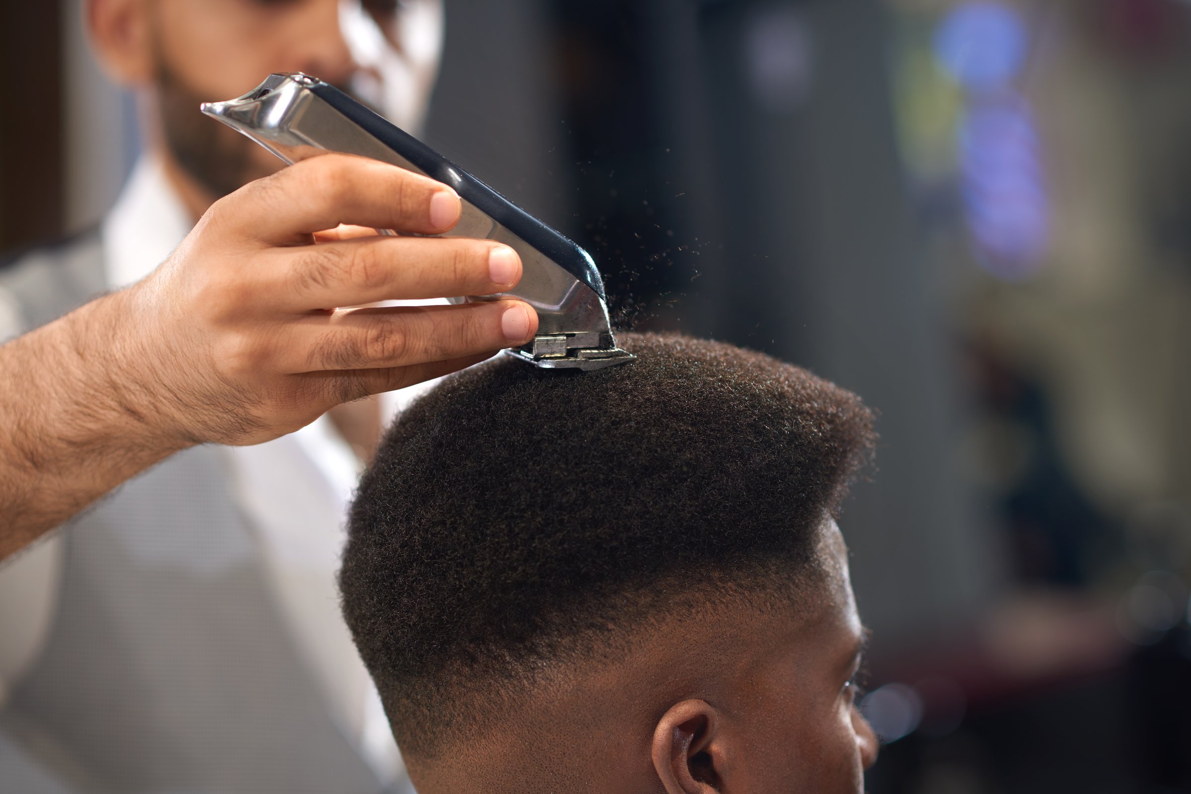 Closeup of process of trimming of hair in barber shop. Qualified barber keeping clipper in hands and correcting shape of hair to male client sitting on chair. Concept of haircut and shaving.