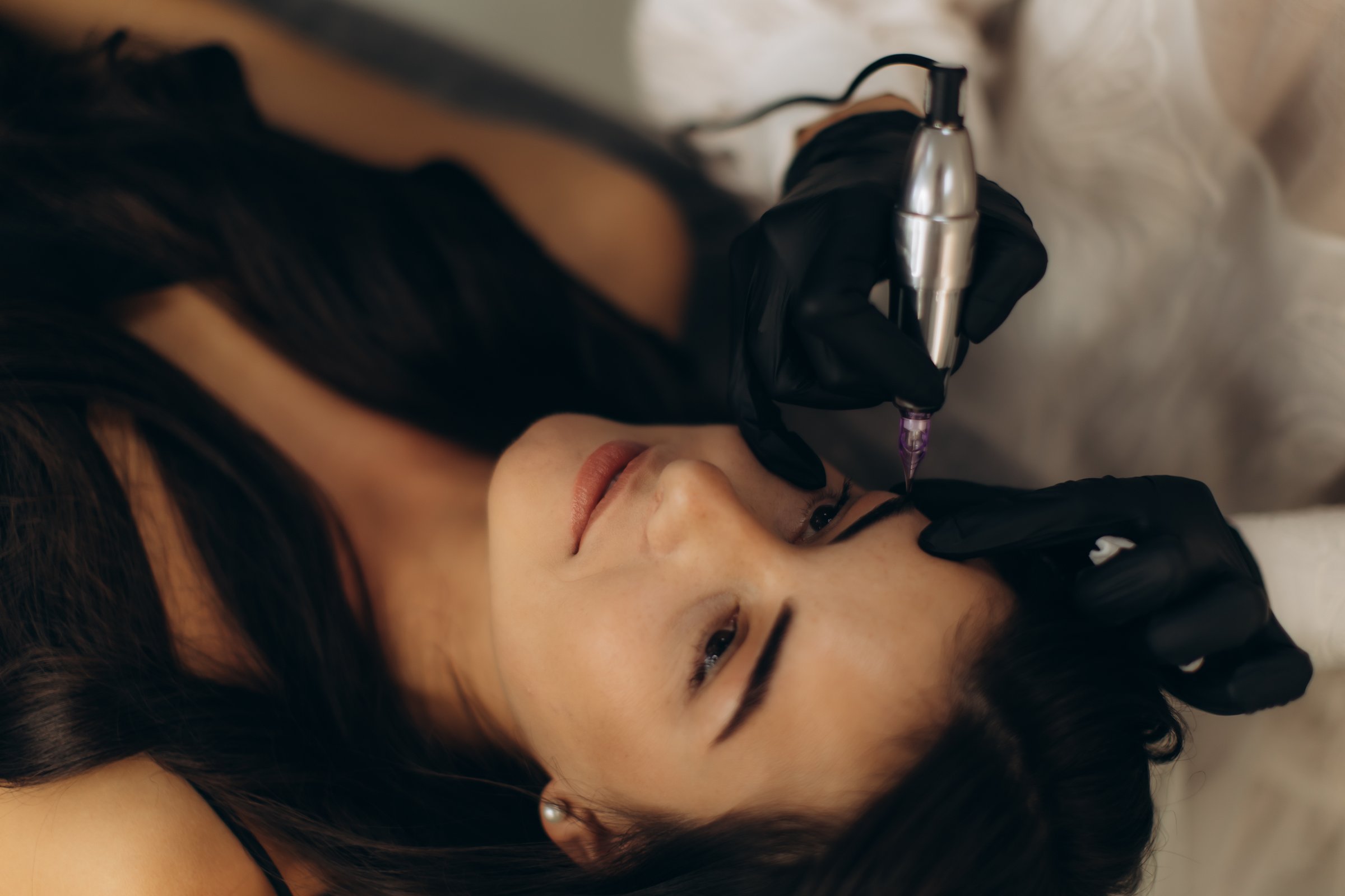 Cosmetologist performing microblading eyebrow tattoo procedure on a young woman in a modern beauty salon, precise shaping and care