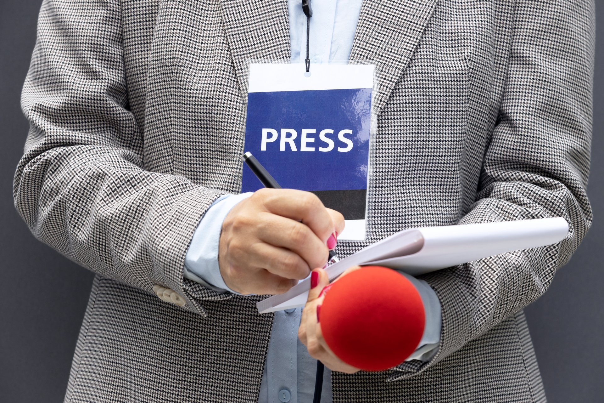 Female reporter at news conference or media event, writing notes, holding microphone