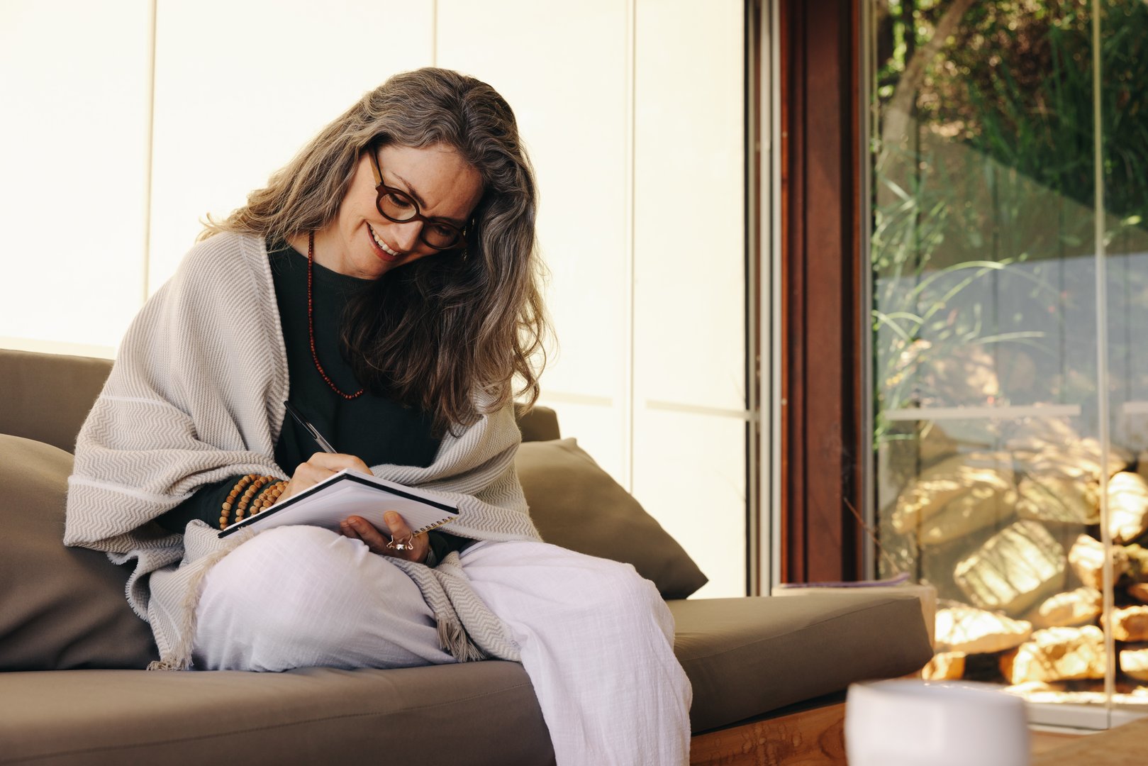 Journaling during retirement. Mature woman smiling happily while writing in her journal at home. Cheerful senior woman writing down her thoughts while sitting on a couch.