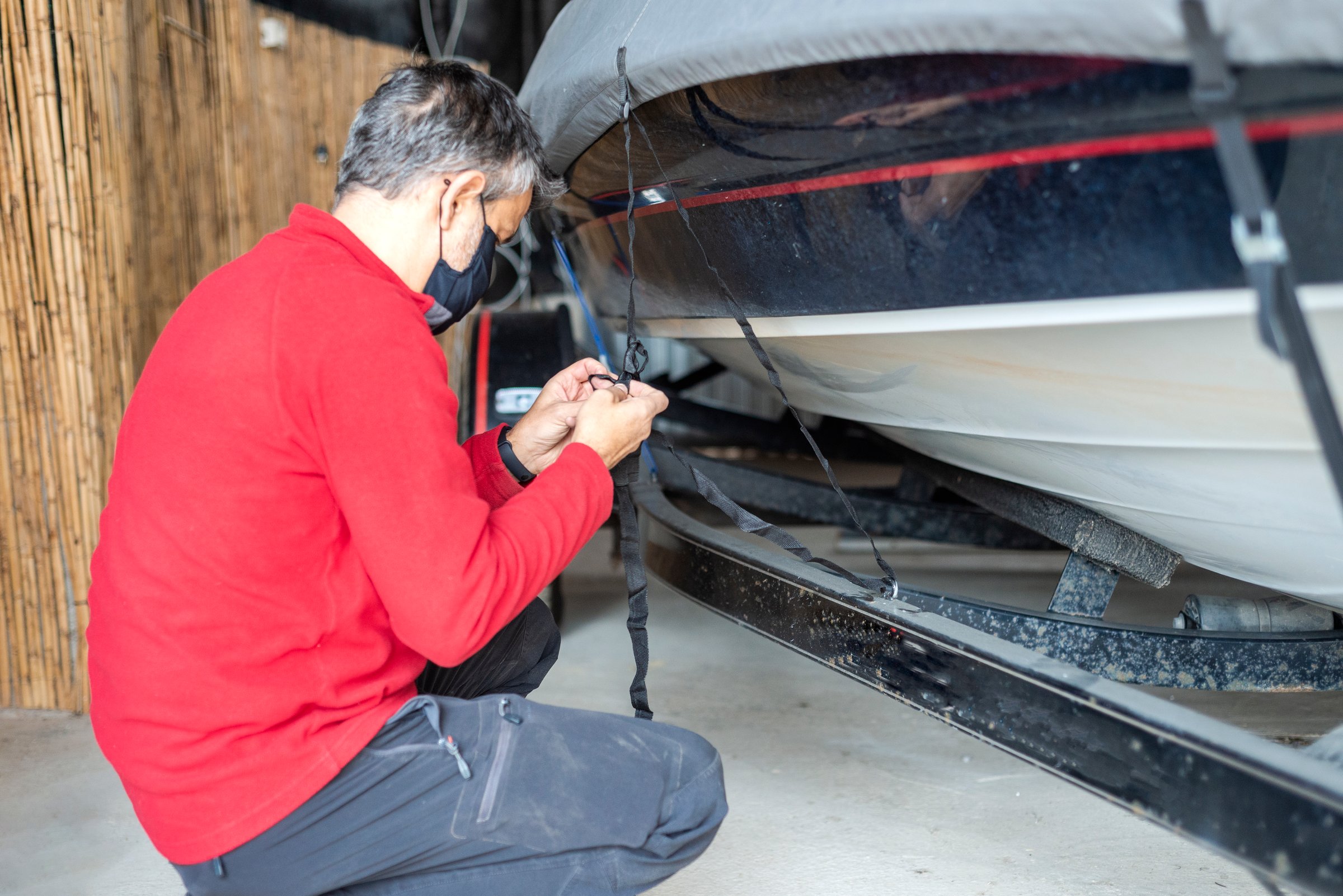 An adult male with a protective mask checks the fastening straps of a motorboat in the garage