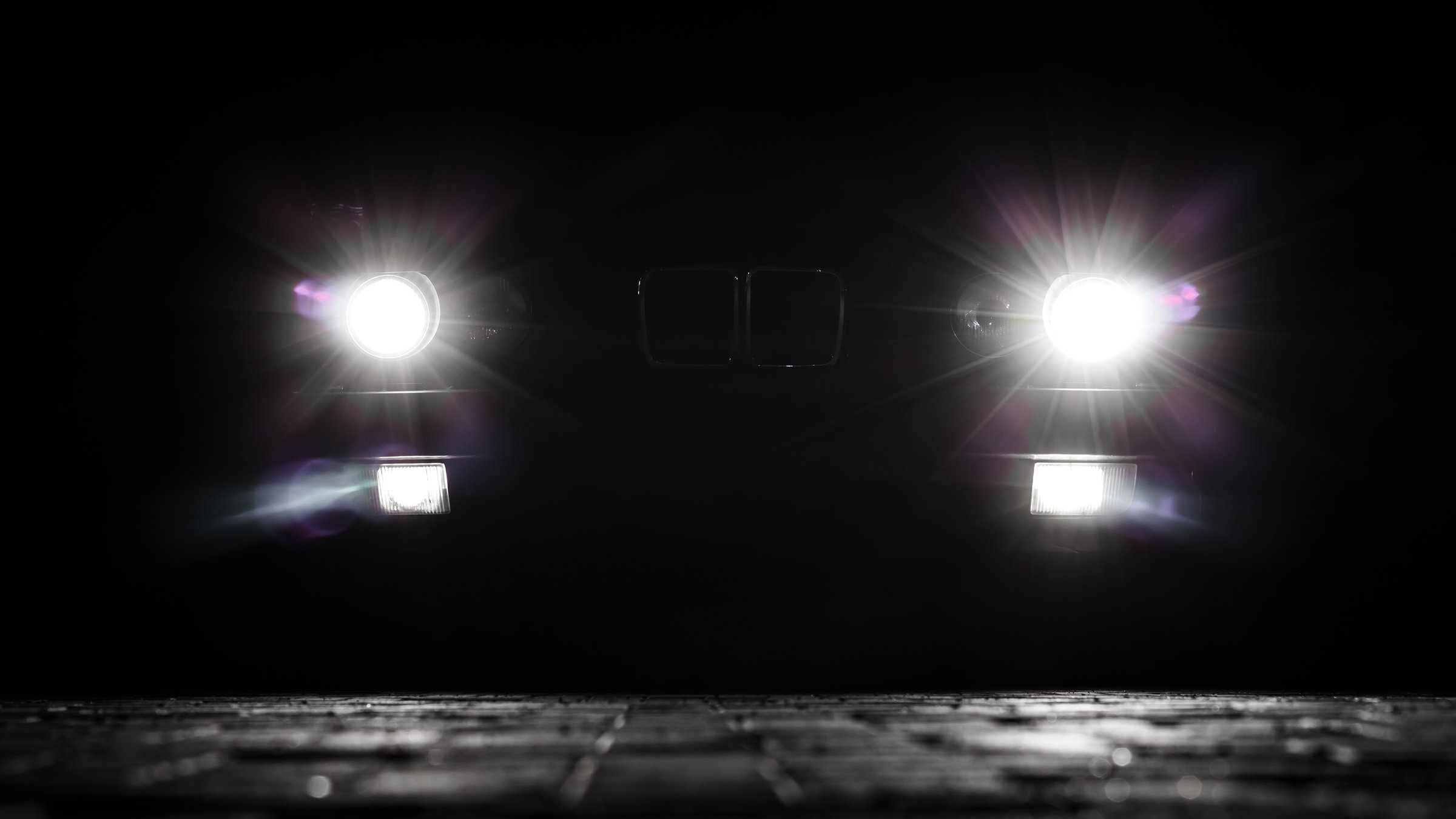 Bright headlights of a vintage car cutting through the darkness at night. Beams and lens flares on the asphalt. Stylized night shot.