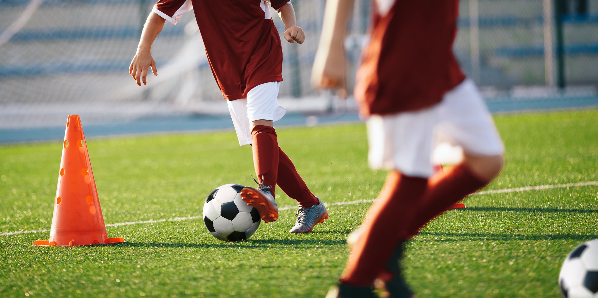Boys running soccer balls between training cones. European football sports summer camp for youth athletes. Soccer boys with balls on grass pitch. Soccer goal and stadium in the background