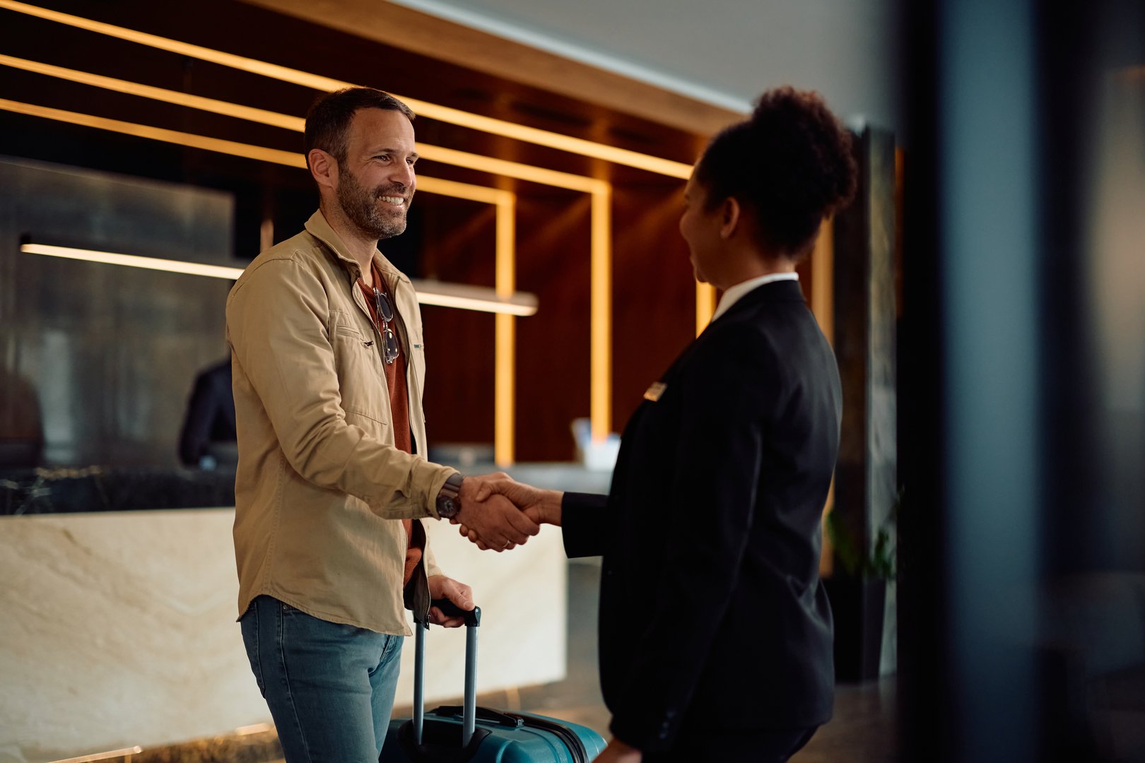 Happy hotel guest and African American female concierge greeting in a lobby.