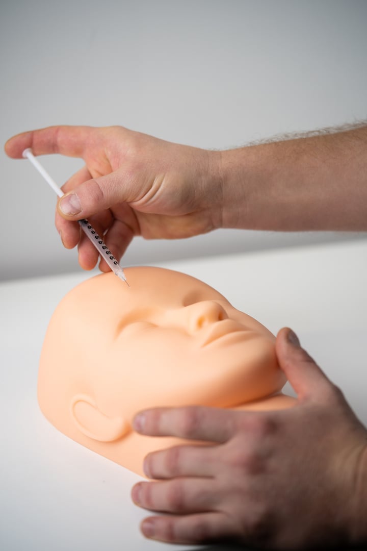 a cosmetologist trains to inject a cosmetic syringe into the face of a rubber mannequin