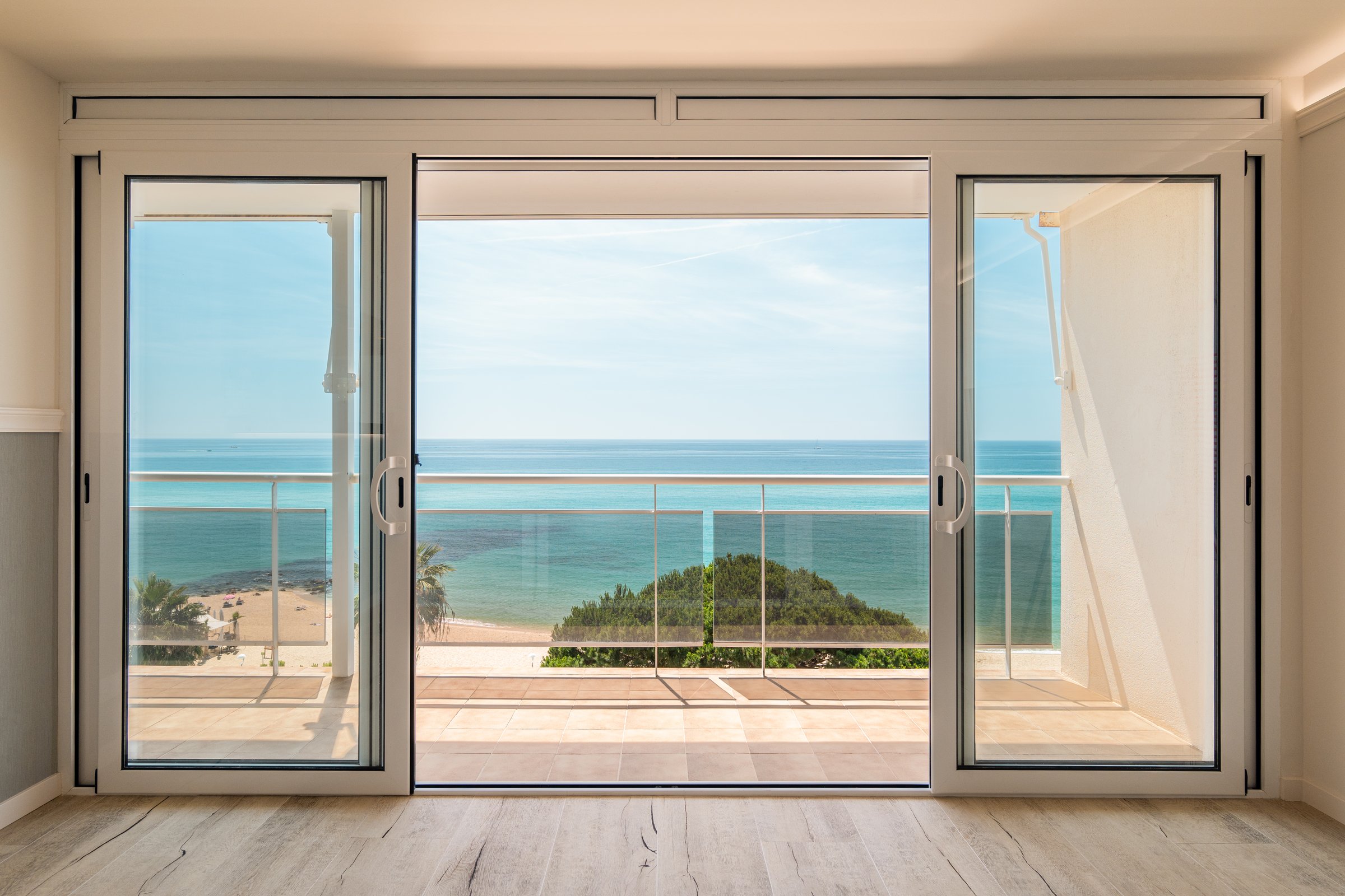 Picturesque view from a guest house through panoramic window with terrace to the sea on a sunny warm summer day with blue skies in a luxury resort. Concept of a room in a five-star hotel.