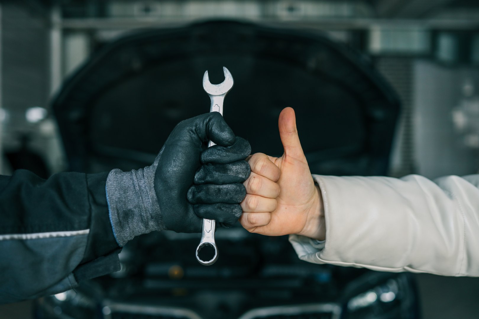 Close-up of a mechanic's gloved hand holding a wrench and a customer's hand giving a thumbs-up, symbolizing satisfaction and trust in car repair services.
