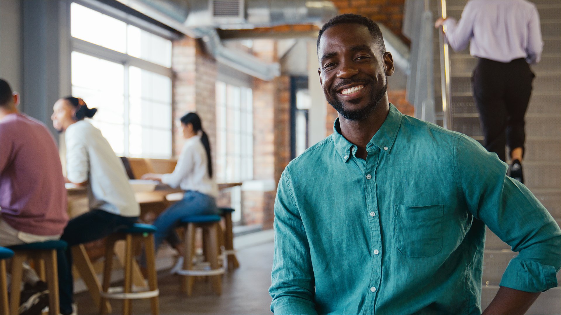 Portrait Of Smiling Businessman Working In Busy Modern Open Plan Office