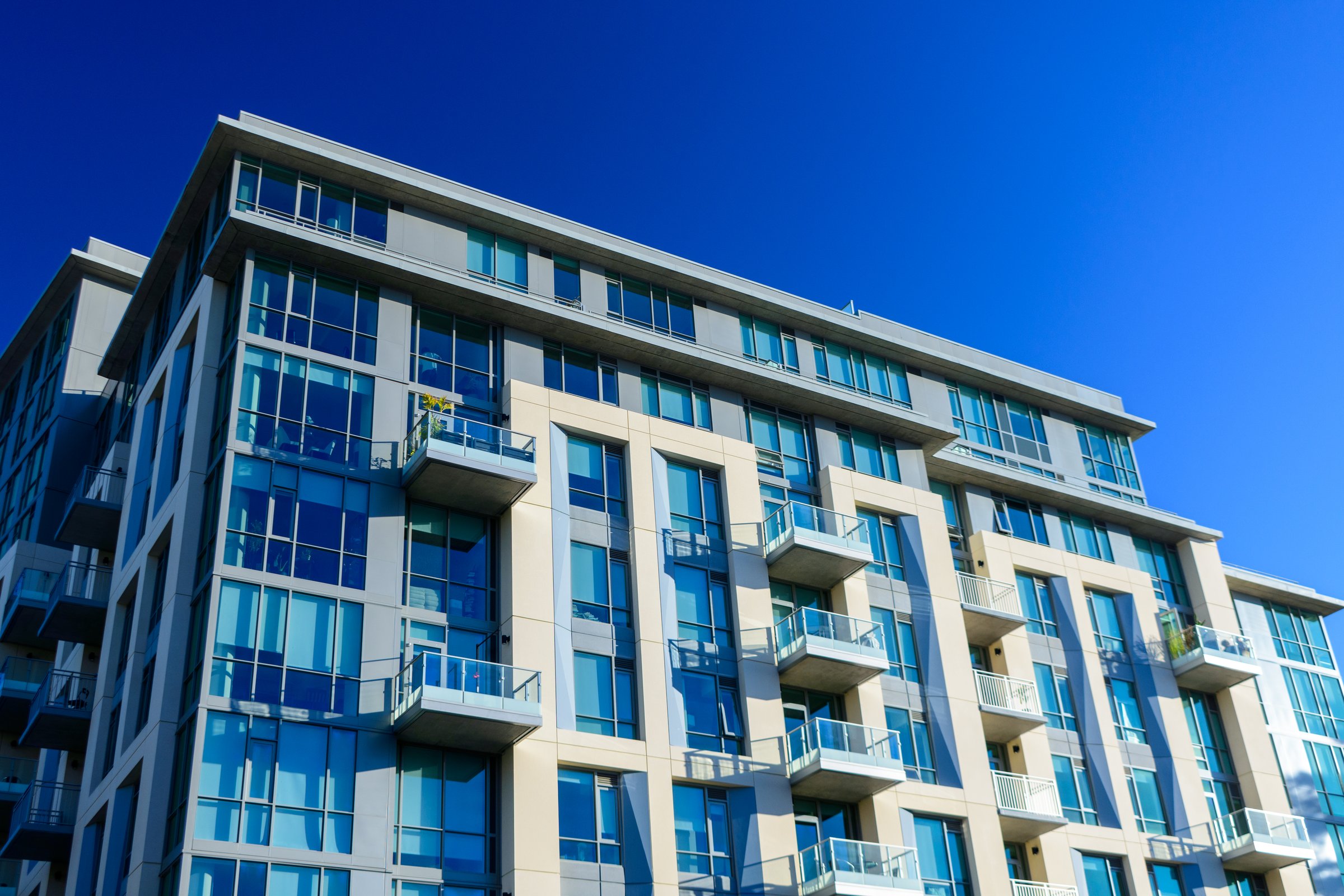 Exterior low-angle view of a modern high-rise apartment building with large glass windows and balconies.