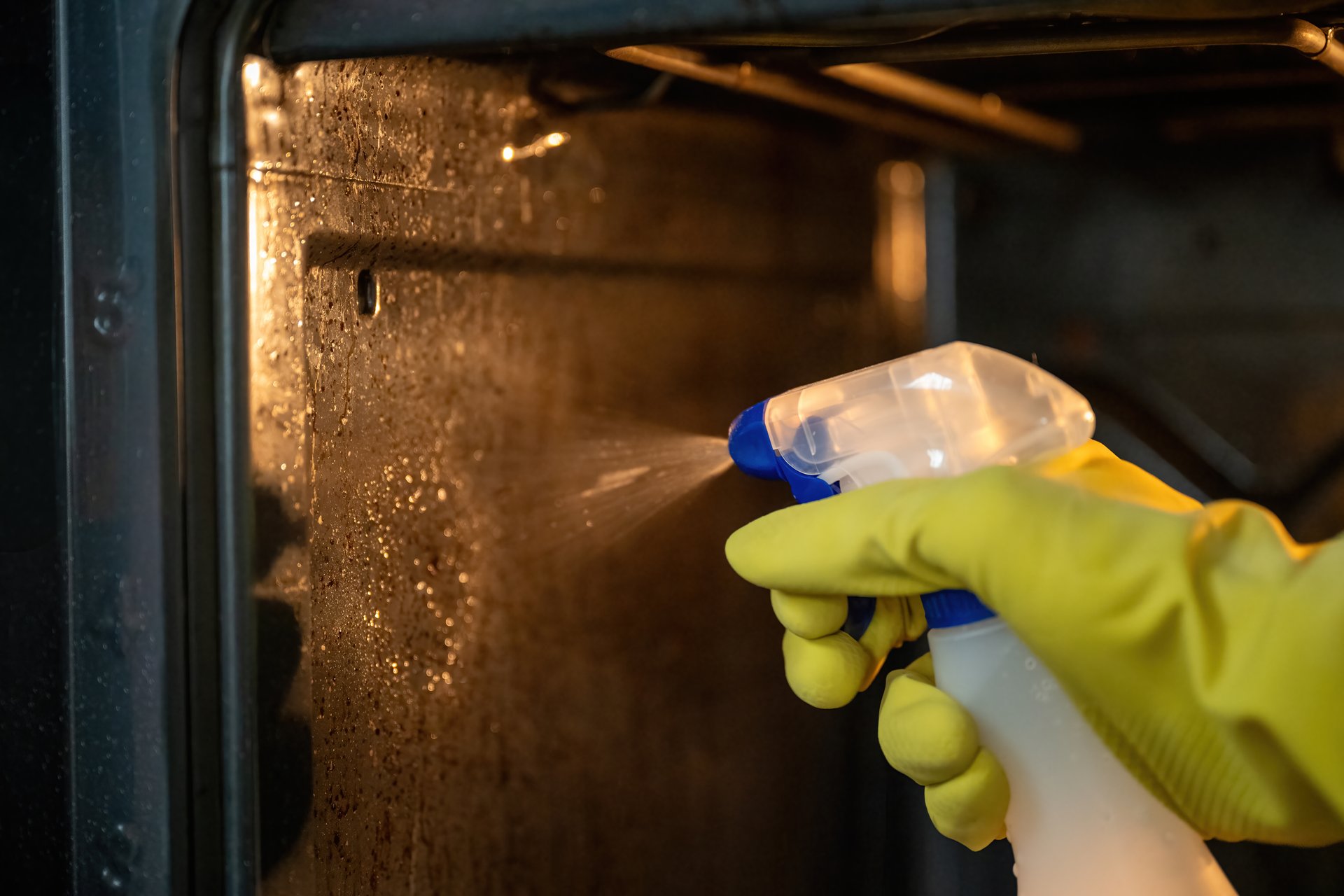 Person spraying degreaser inside dirty oven with yellow rubber gloves