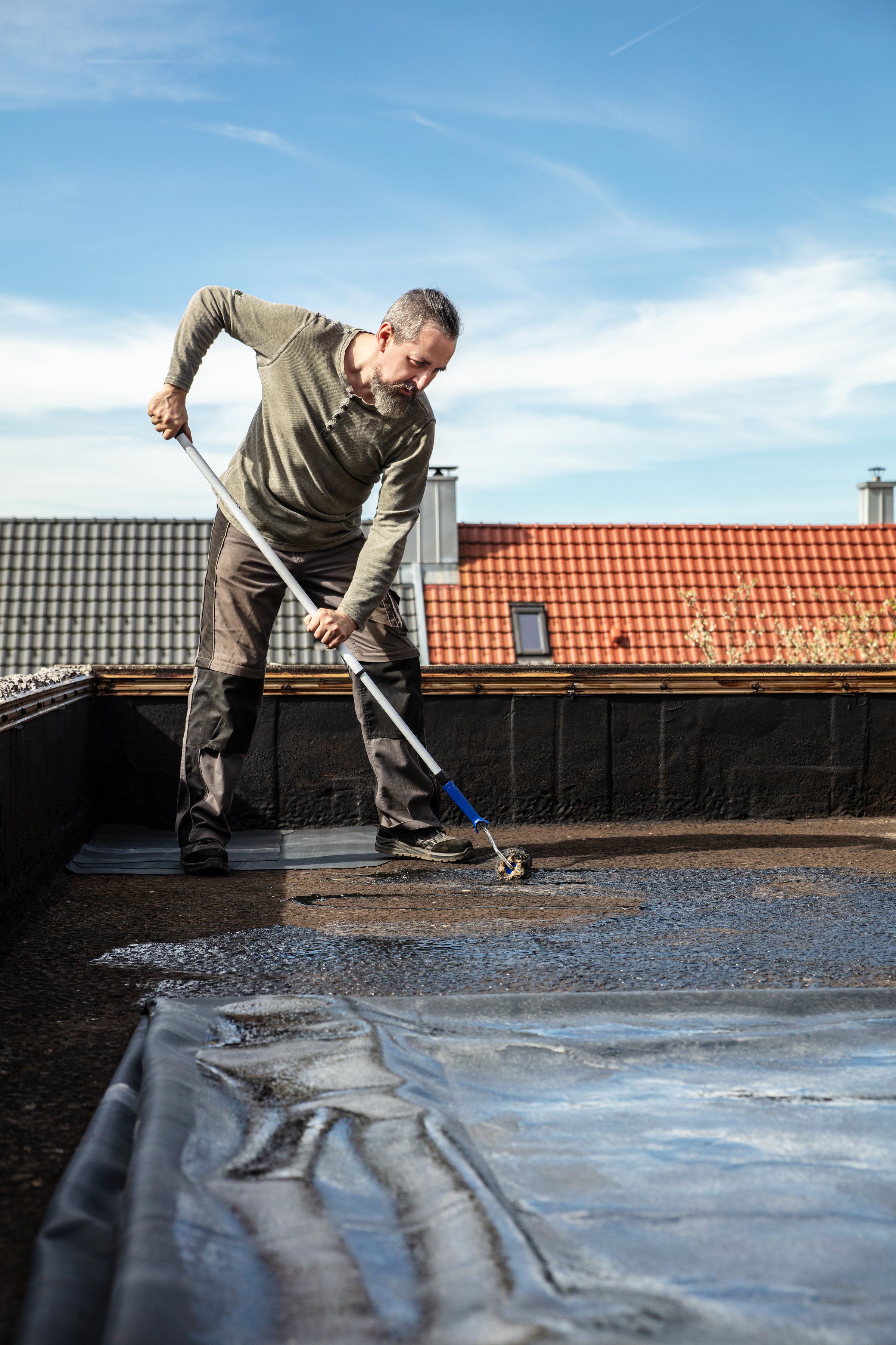 a man applies adhesive to an old bitumen sealant and then glues on a rubber sheet