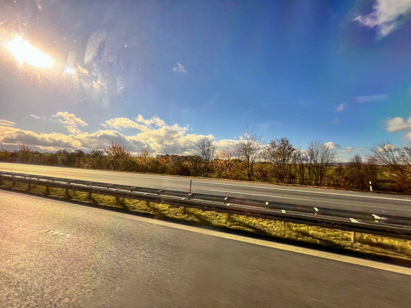 Highway with guardrail and trees under a clear blue sky and sunflare