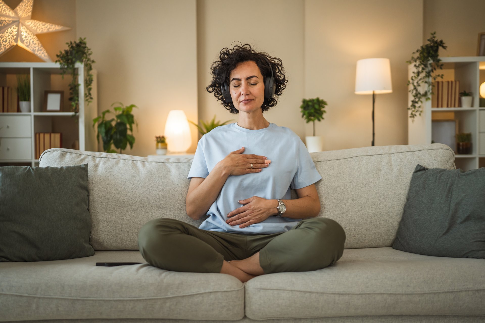 Mature woman sit on sofa with headphones and have guided meditation