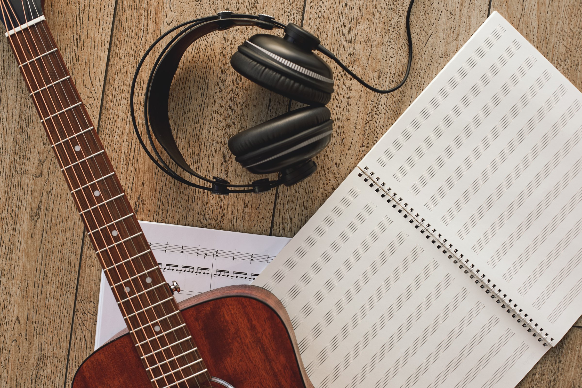 Close up view of guitar, professional headphones and musical notes laying on the wooden floor. Musical instruments. Music equipment