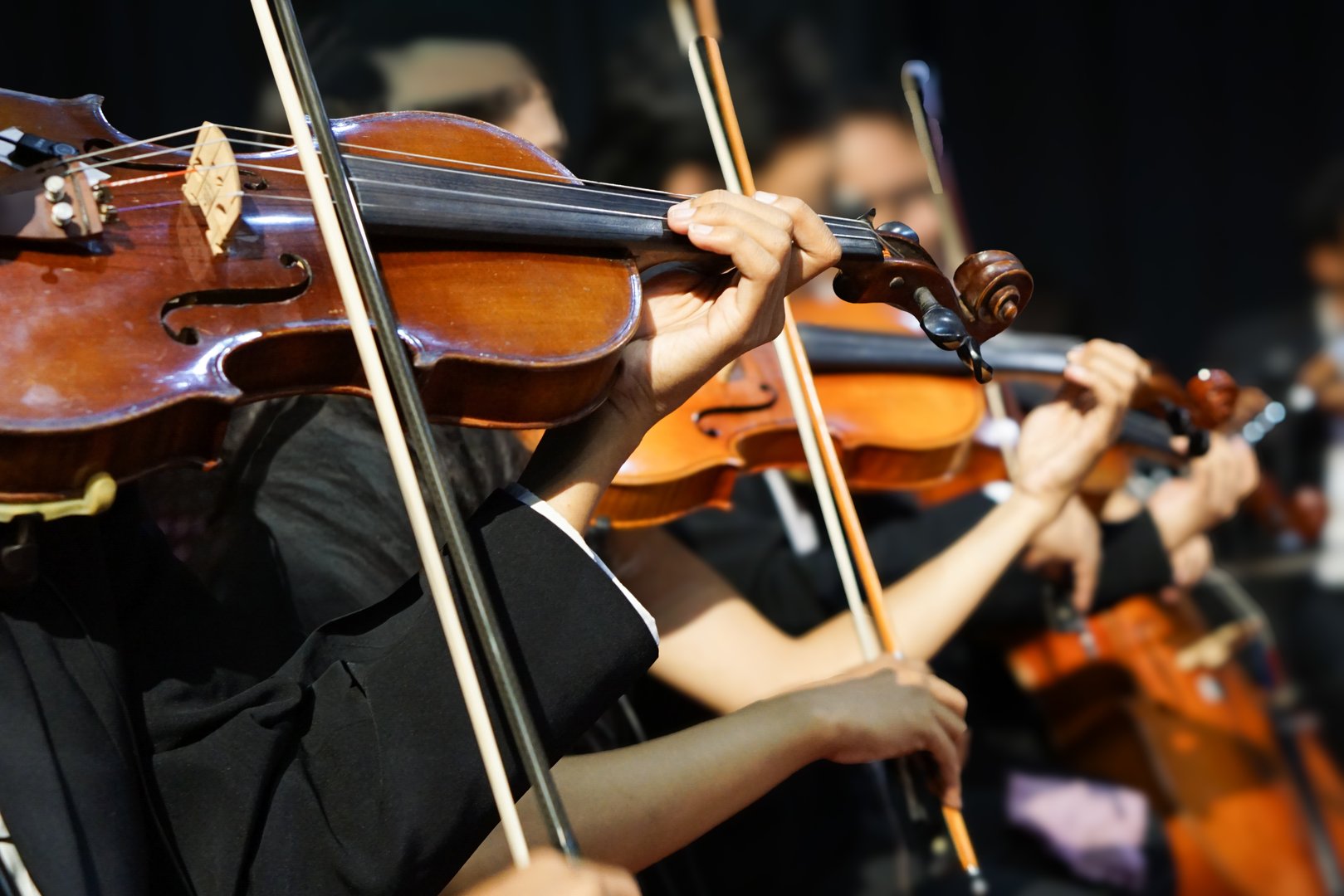 Hands playing violin orchestra with note sheet on stage.