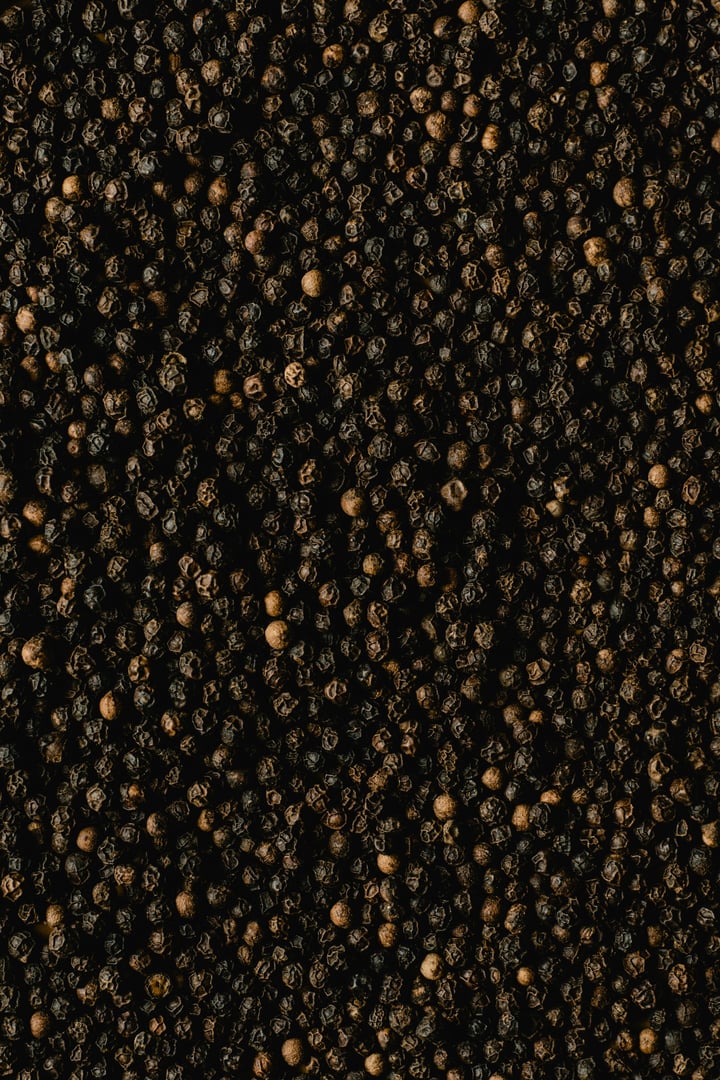 Close-up of a pile of black peppercorns, densely packed and uniformly spread across the image.