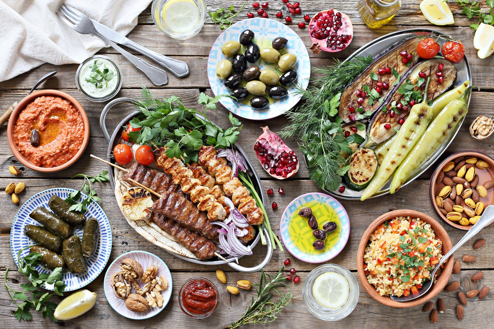 Middle eastern, arabic or mediterranean dinner table with grilled lamb kebab, chicken skewers  with roasted vegetables and appetizers variety serving on rustic outdoor table. Overhead view.