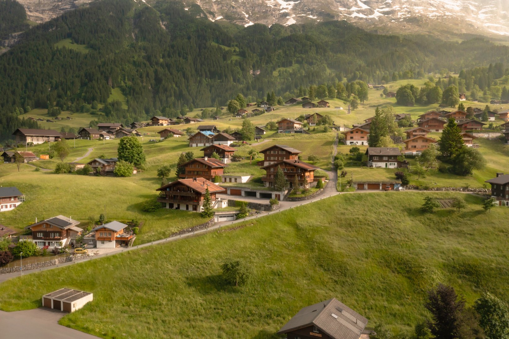 Drone view capturing the Grindelwald mountain village nestled in the Bernese Oberland, surrounded by alpine peaks and lush greenery.