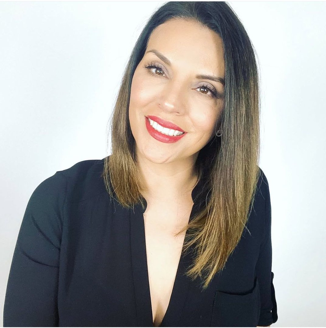 Woman with shoulder-length hair and red lipstick smiling in a black top against a plain white background.