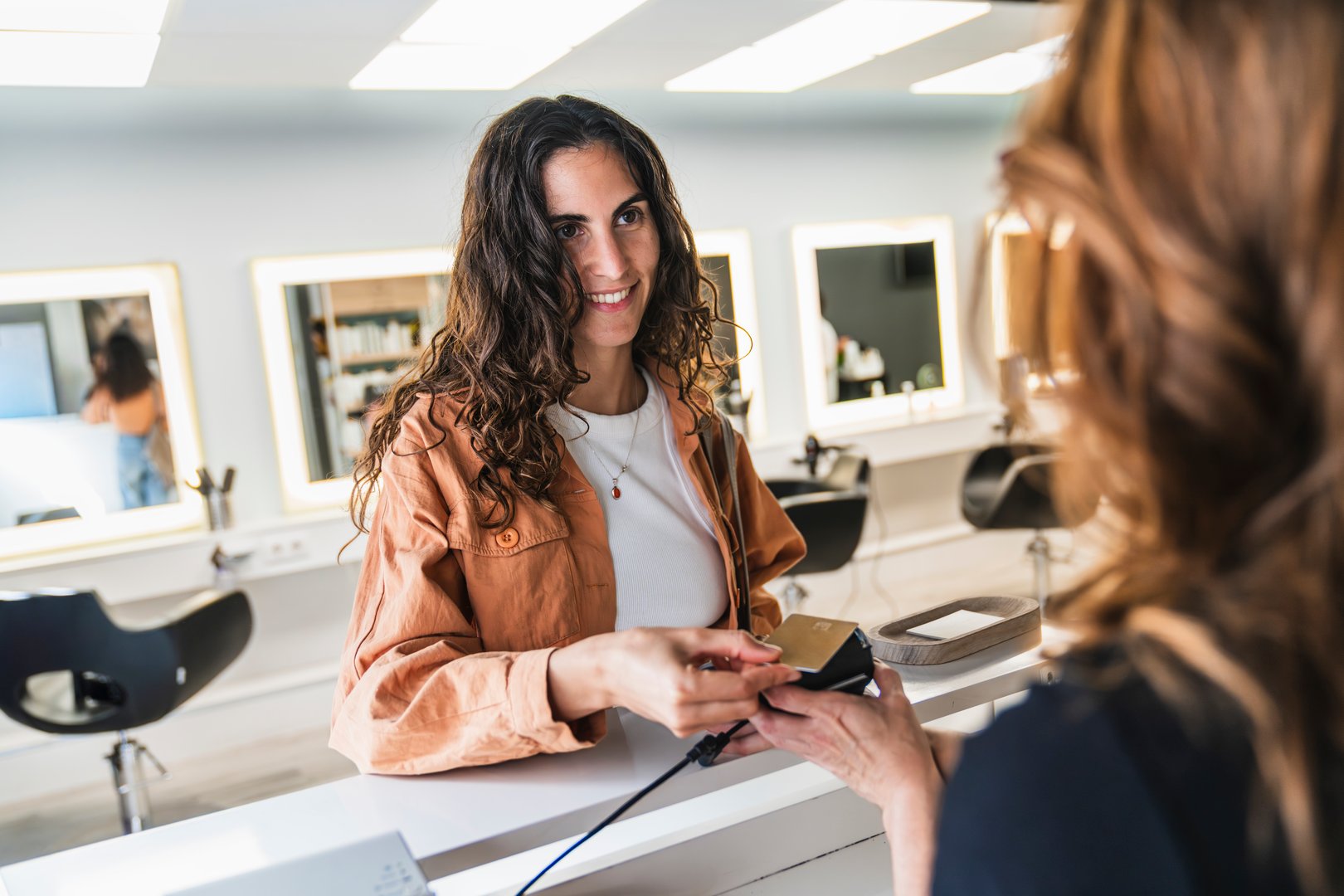 Smiling customer making a contactless payment with a credit card at the reception desk of a modern hair salon