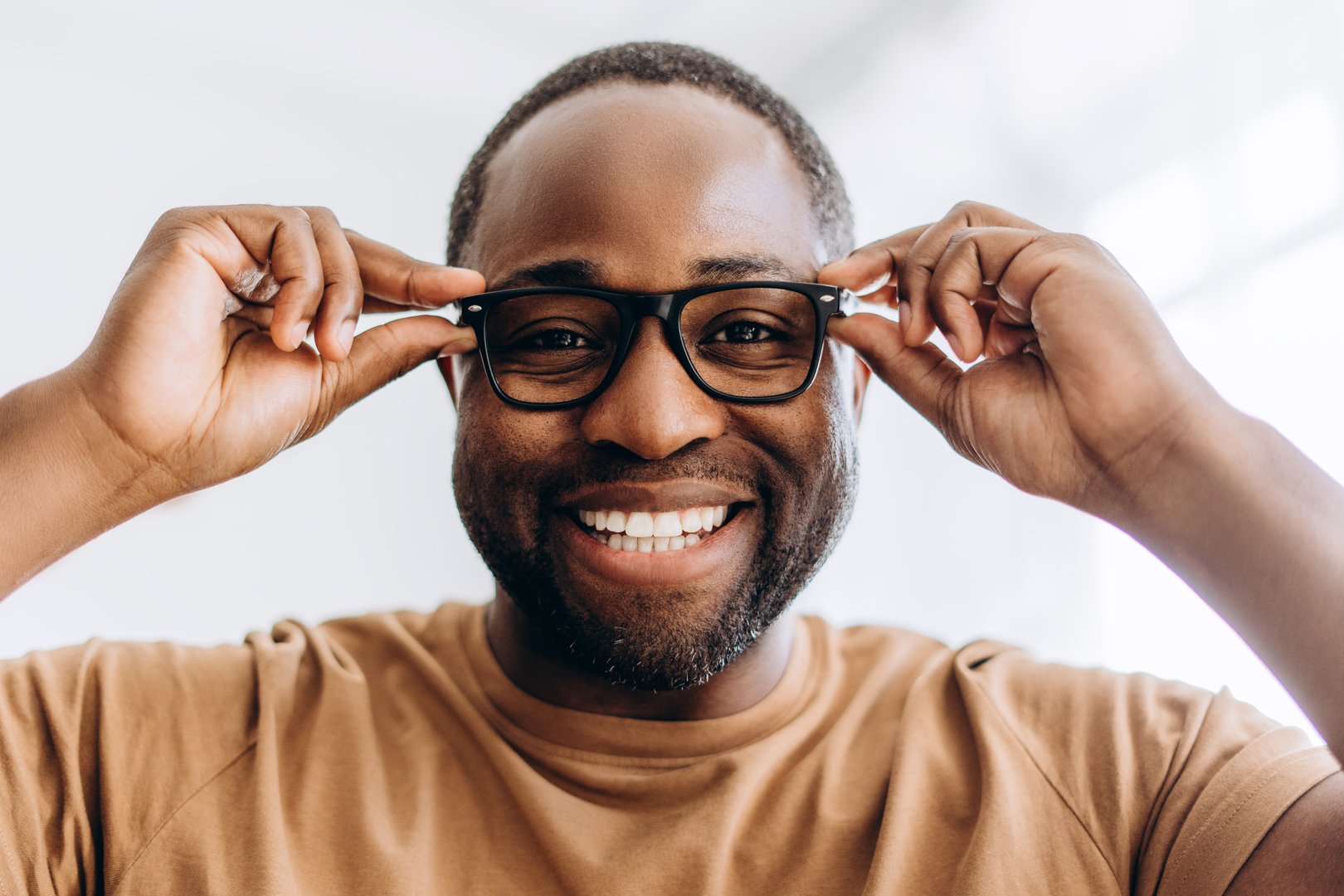 Smiling young African American guy posing at camera wearing stylish black glasses