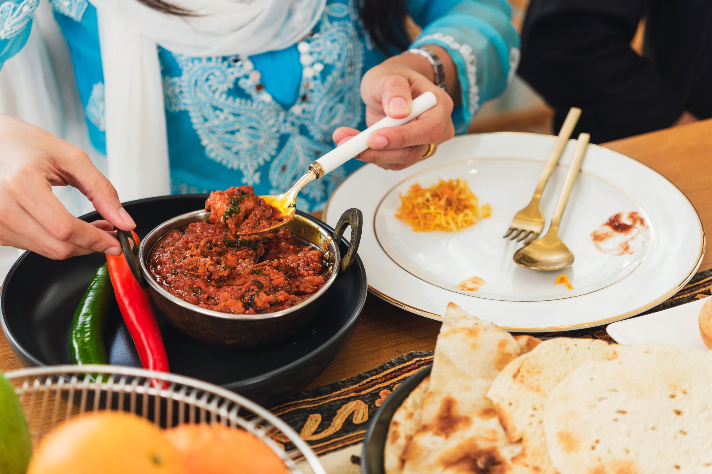 A person serves a flavorful Indian or Pakistani curry dish with naan and rice at a traditional meal. Rich spices, vibrant colors, and authentic cuisine highlight the essence of South Asian dining.