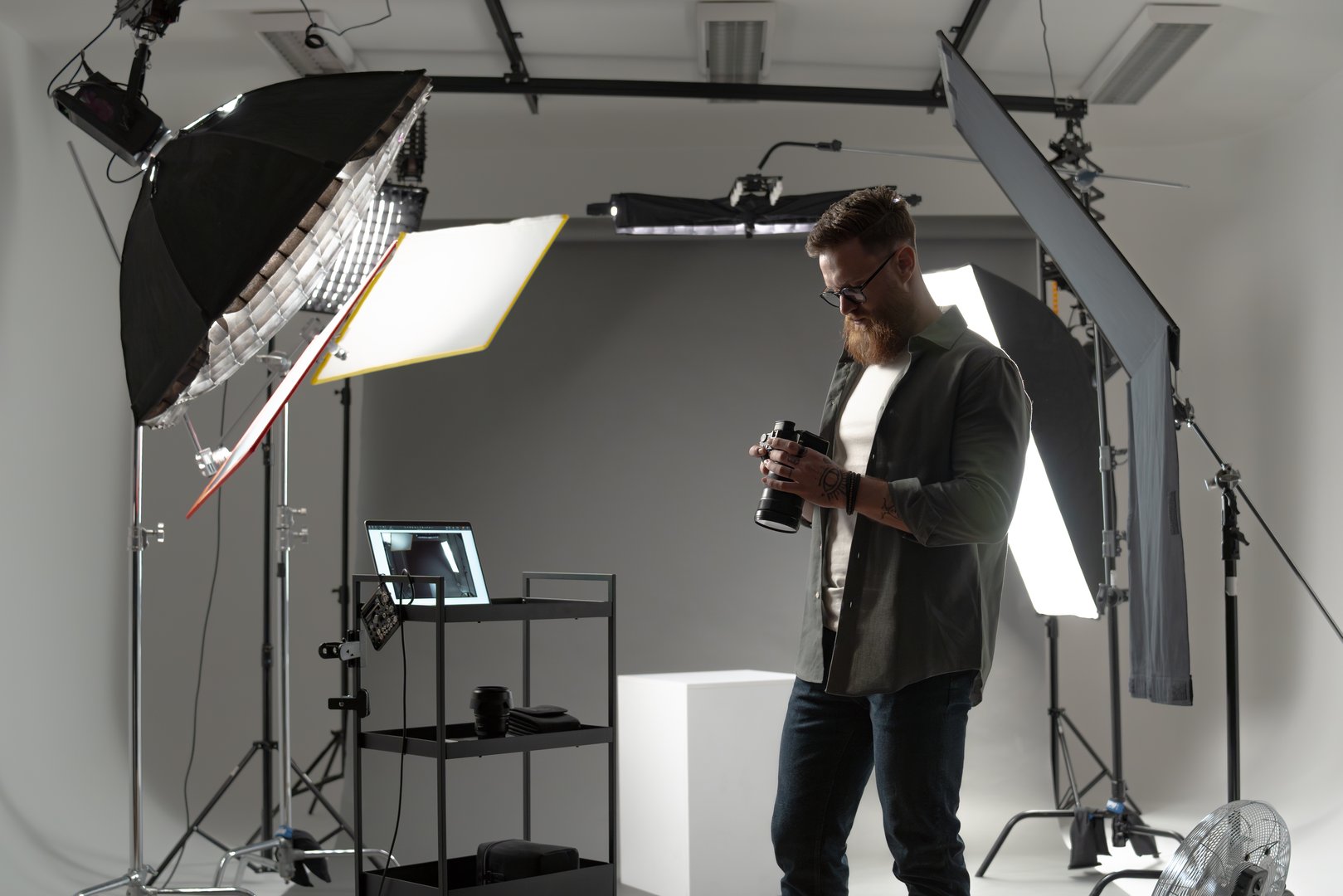 A professional photographer working with camera equipment in a well-equipped studio with lighting setup.
