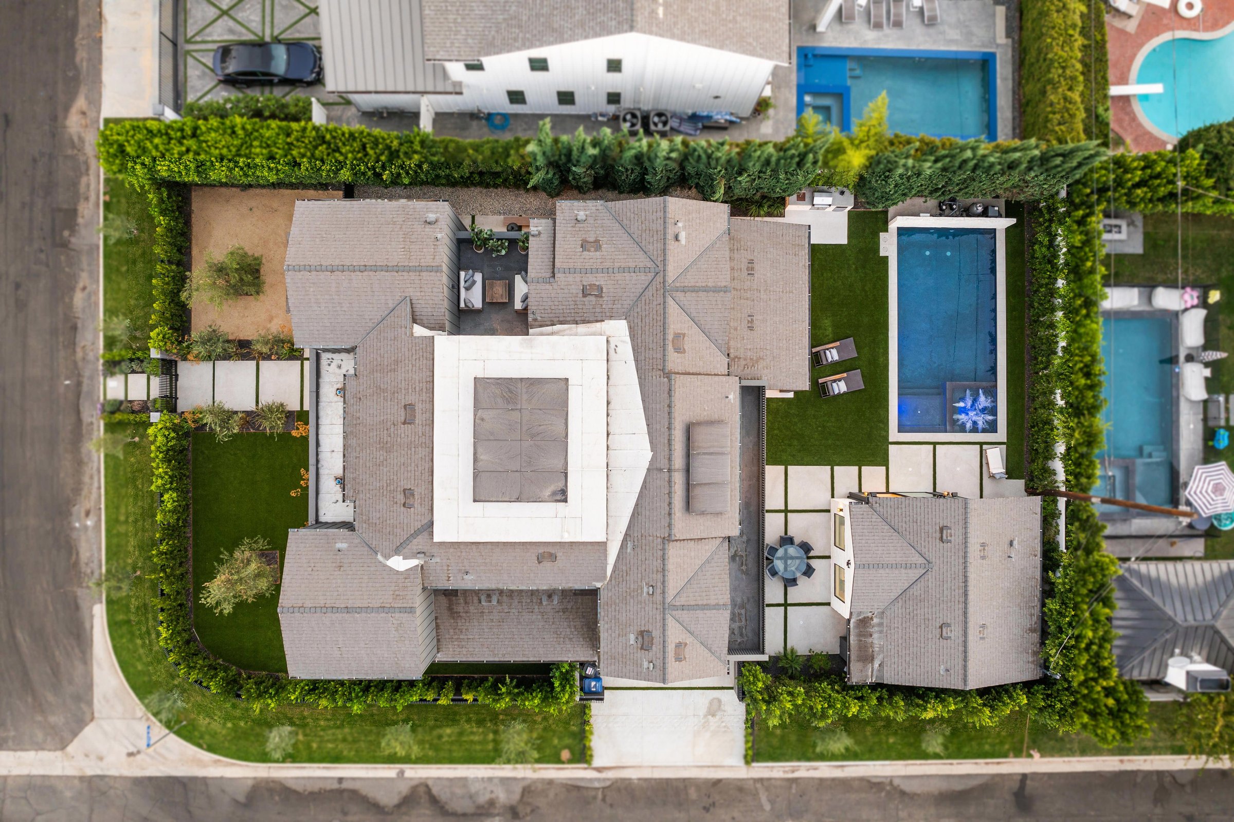 Aerial view of a modern suburban house with a pool, lush garden, and driveway, showcasing contemporary architecture and landscaping.